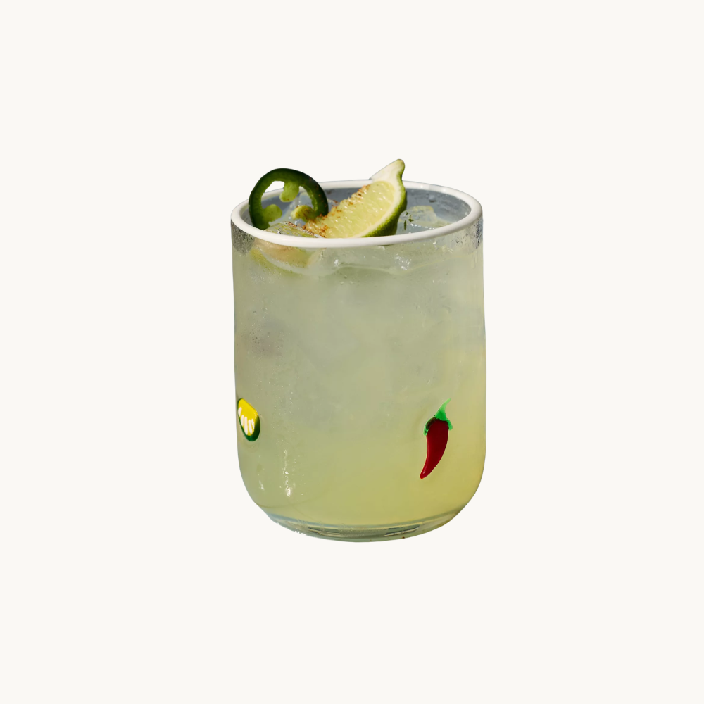 Glass of lime and jalapeño infused cocktail with lime wedge and jalapeño slice garnish, against a white background.