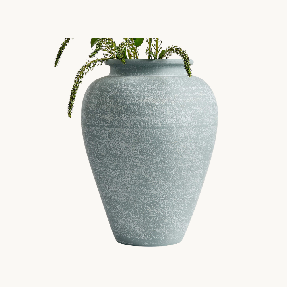 Light green ceramic vase with a textured surface, containing green leafy sprigs.
