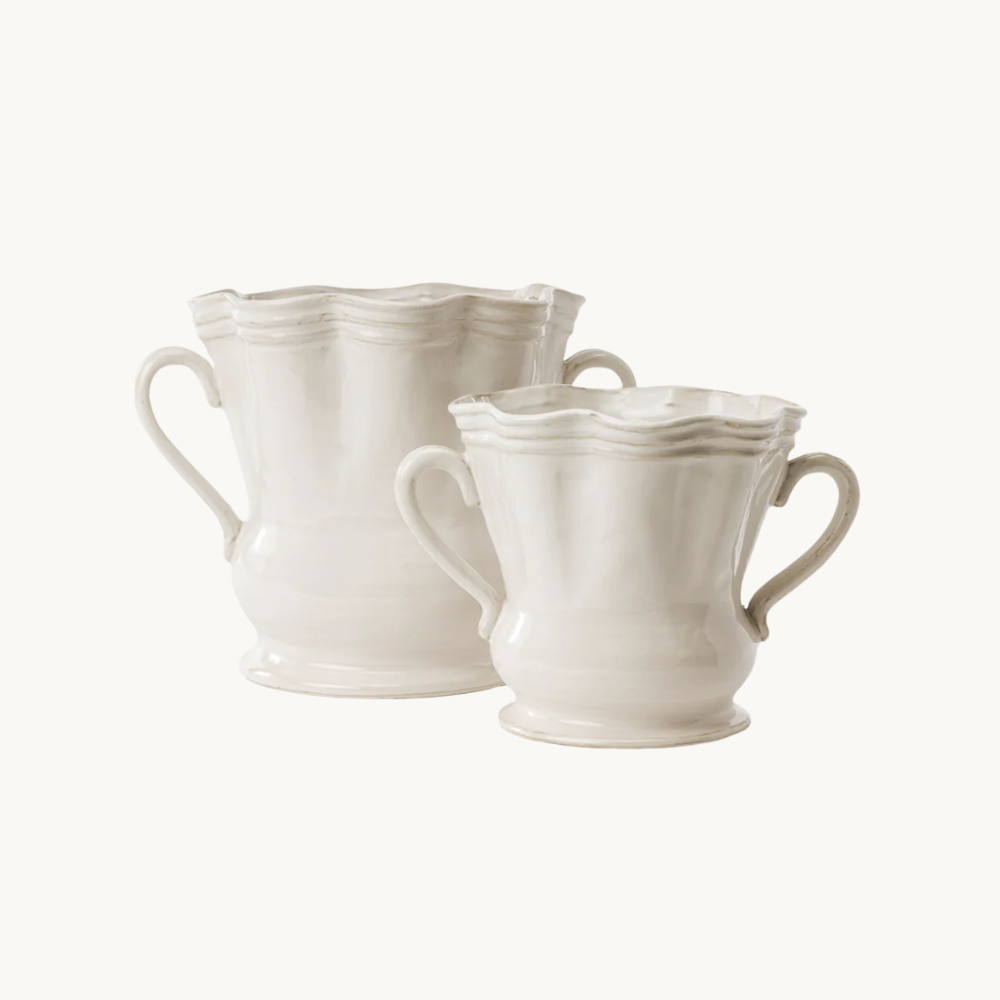 Two white ceramic teacups with wavy rims and handles on a plain background.