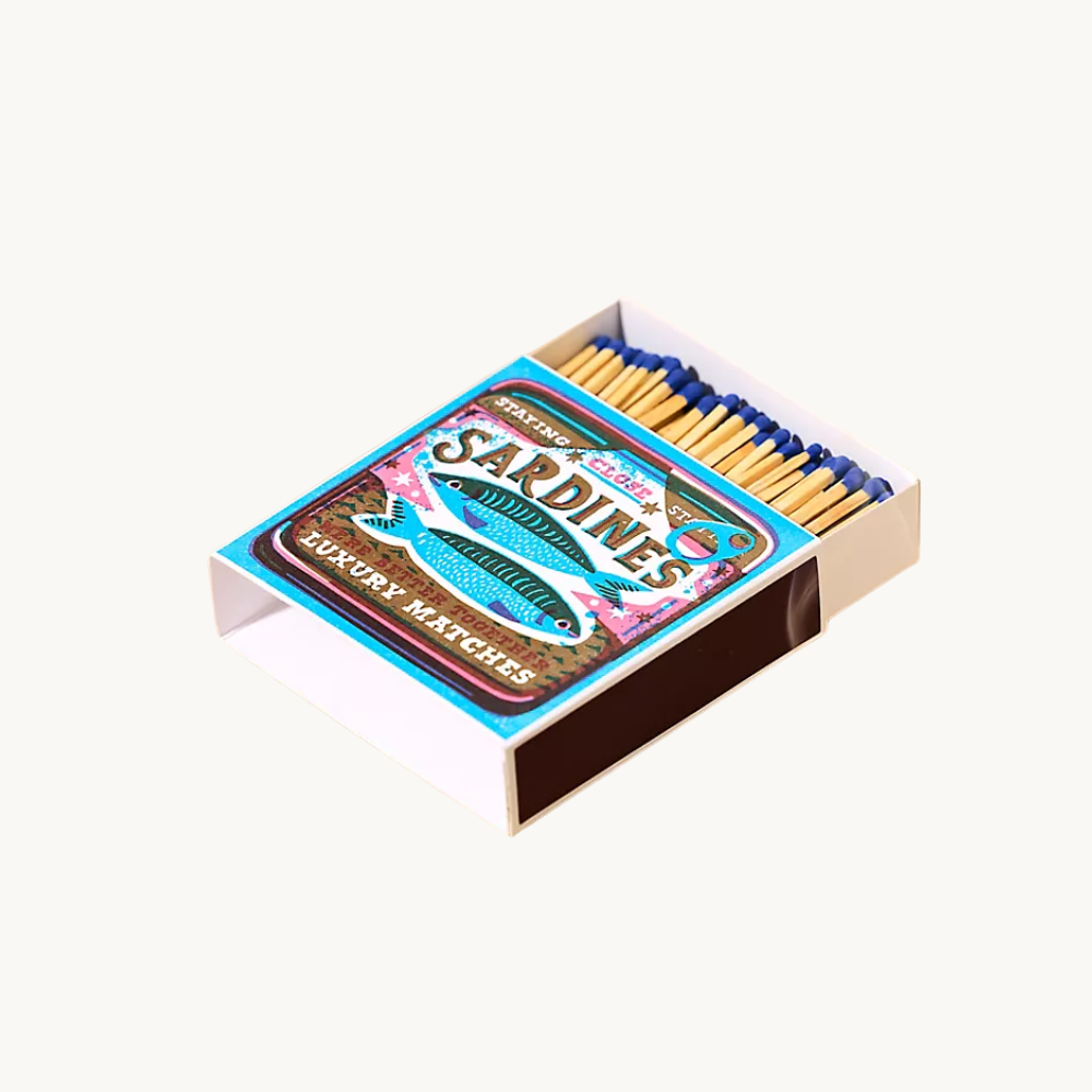 Box of luxury matches with a colorful vintage-style label featuring two blue fish and the text 'Starting Sardines, Luxury Matches'.