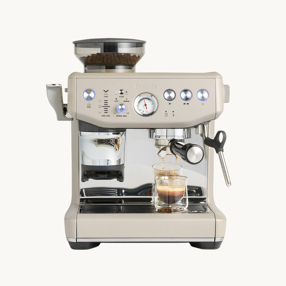 A silver espresso machine brewing coffee into a clear glass cup.