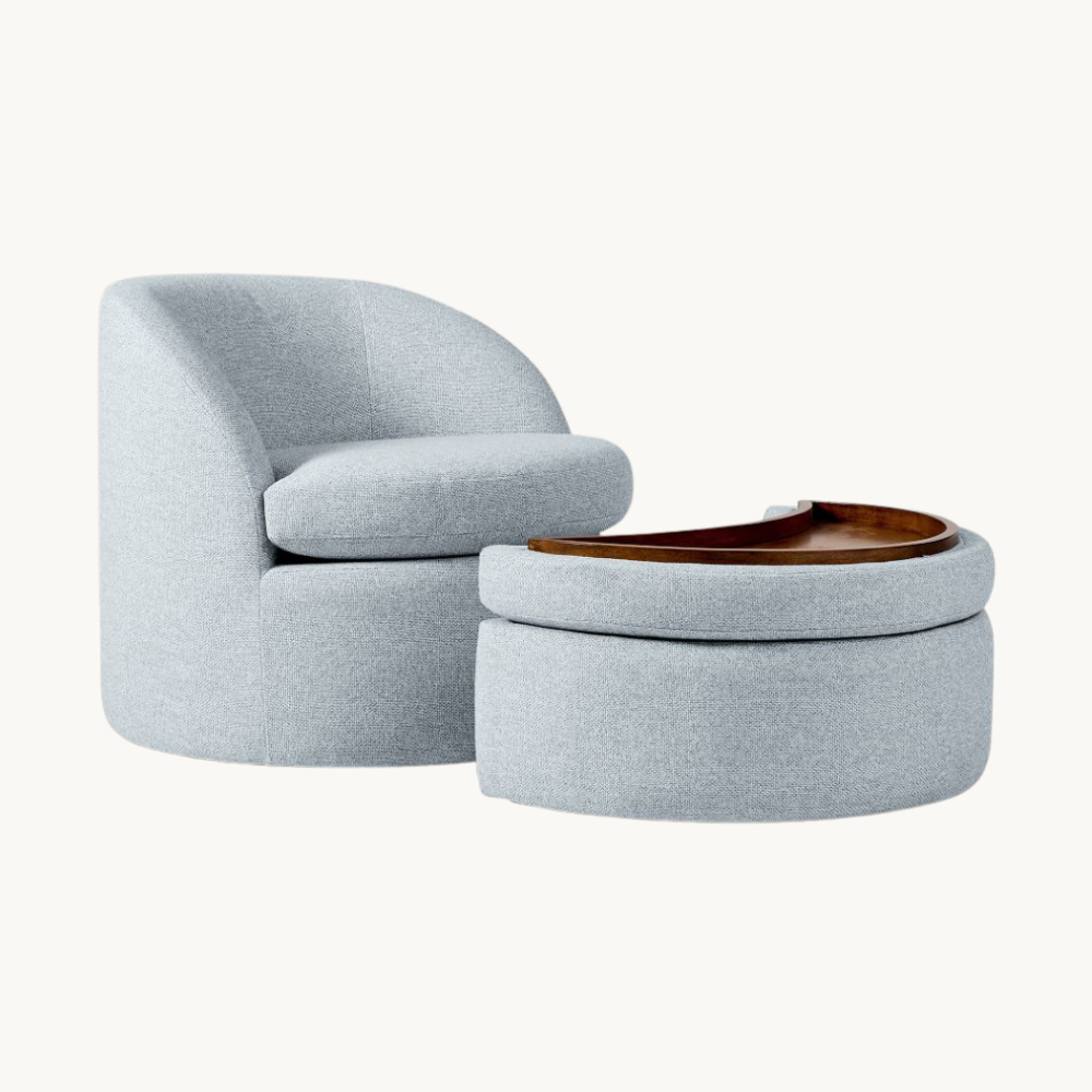 A modern light gray upholstered armchair with a matching round ottoman that has a wooden tray on top, set against a plain white background.