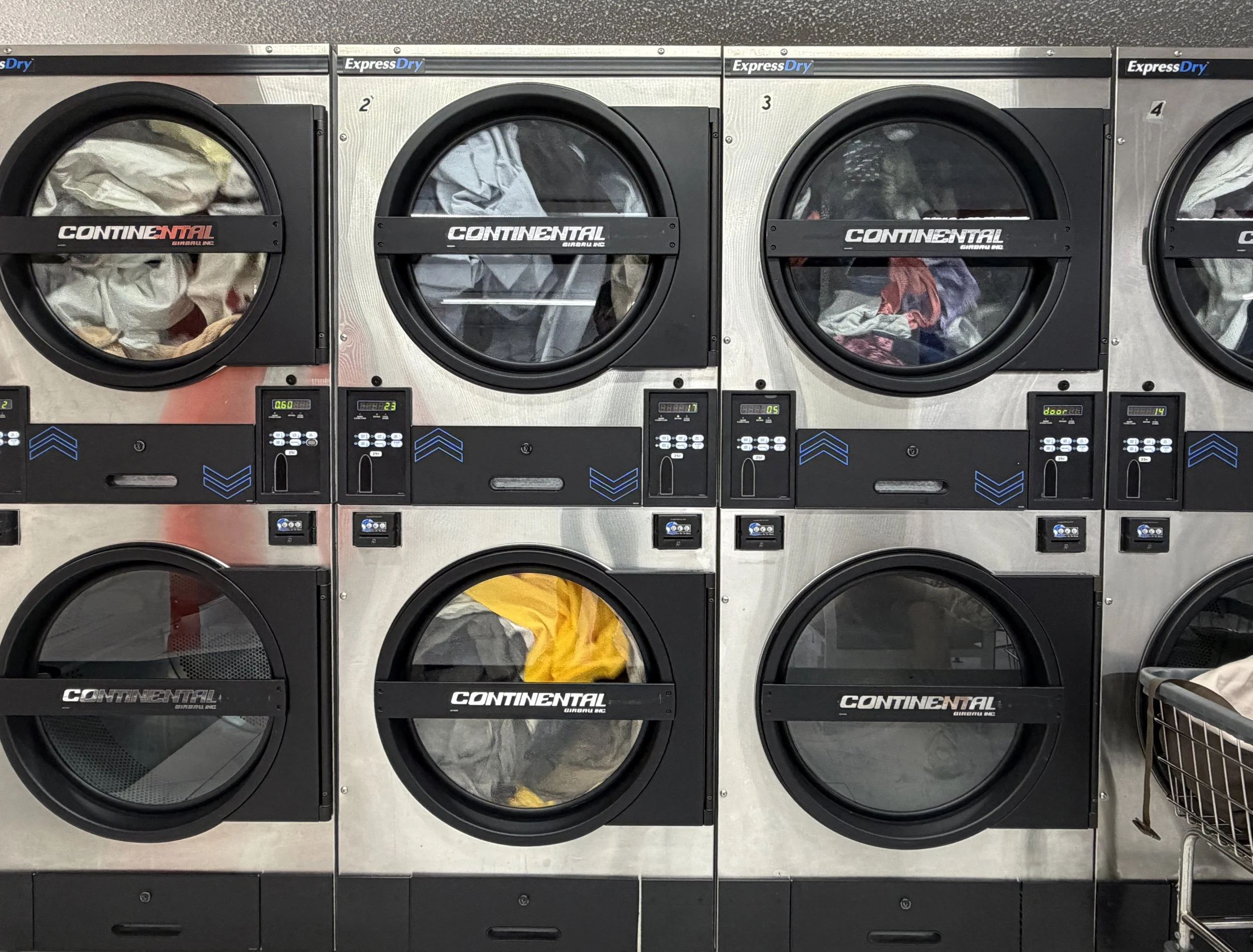 Máquinas de lavandería industriales de carga frontal llenas de ropa usada en diferentes colores y tipos, en un área de lavandería.