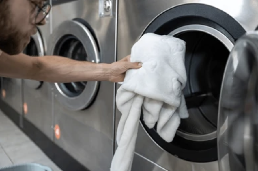 Una persona colocando una prenda de ropa blanca en una lavadora en una lavandería automática.