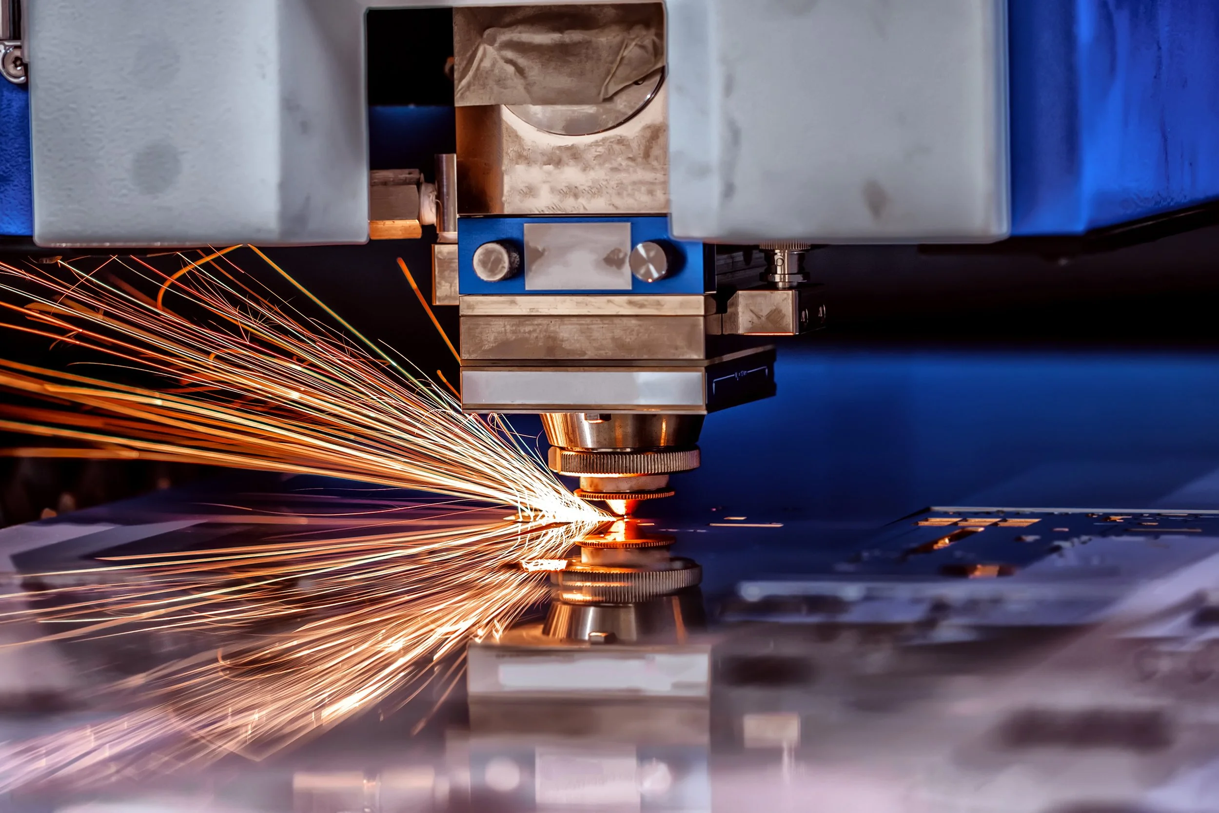 A CNC machine or laser cutter actively cutting metal, with sparks flying from the cutting process.
