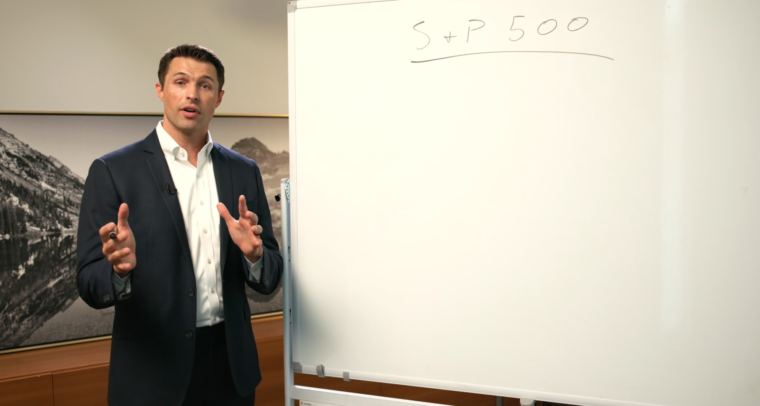 A man in a suit standing beside a whiteboard with writing that says 'S + P 500'.