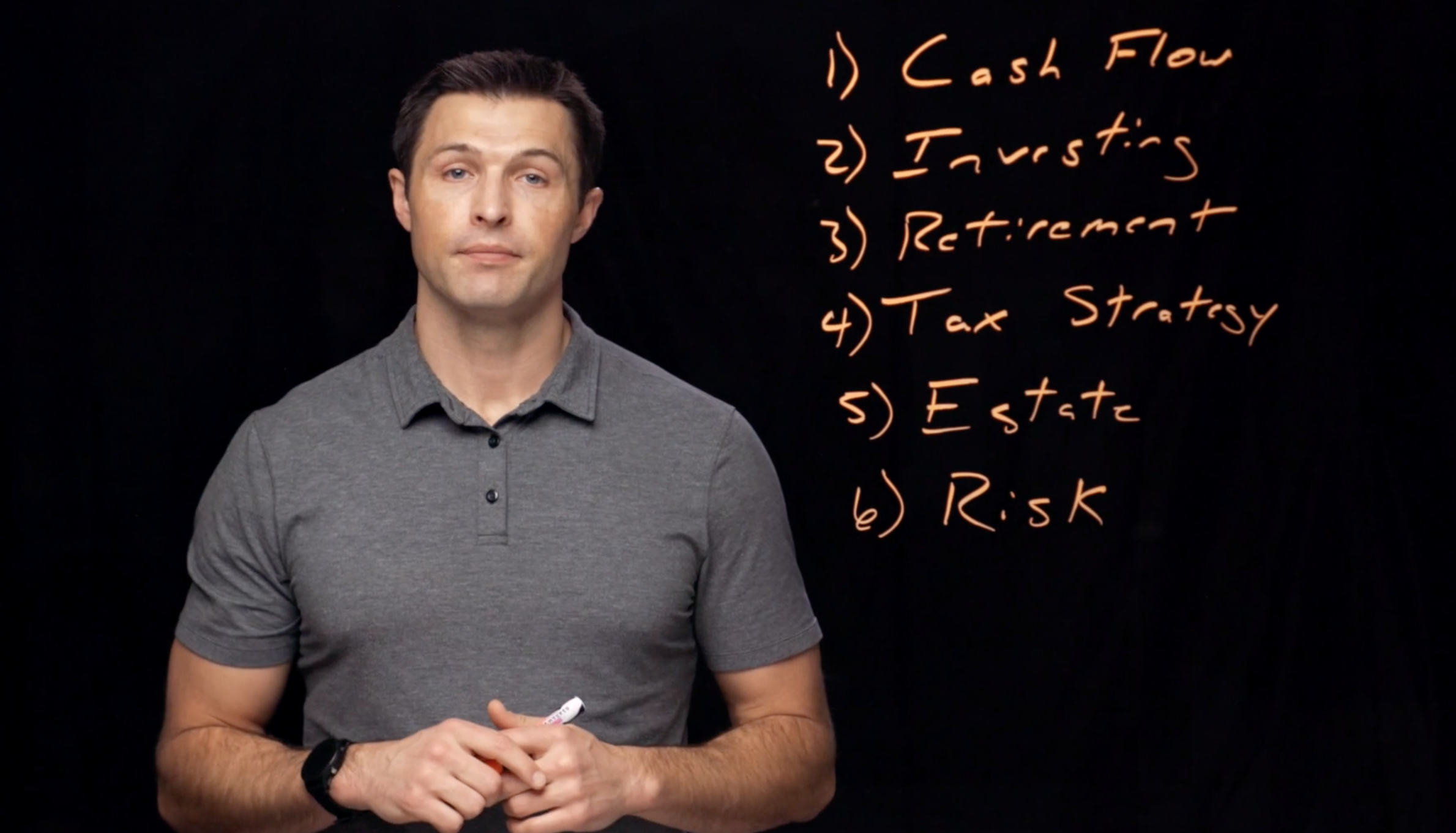 A man in a gray polo shirt holding a marker, standing in front of a blackboard with orange handwritten text listing five points about financial topics.