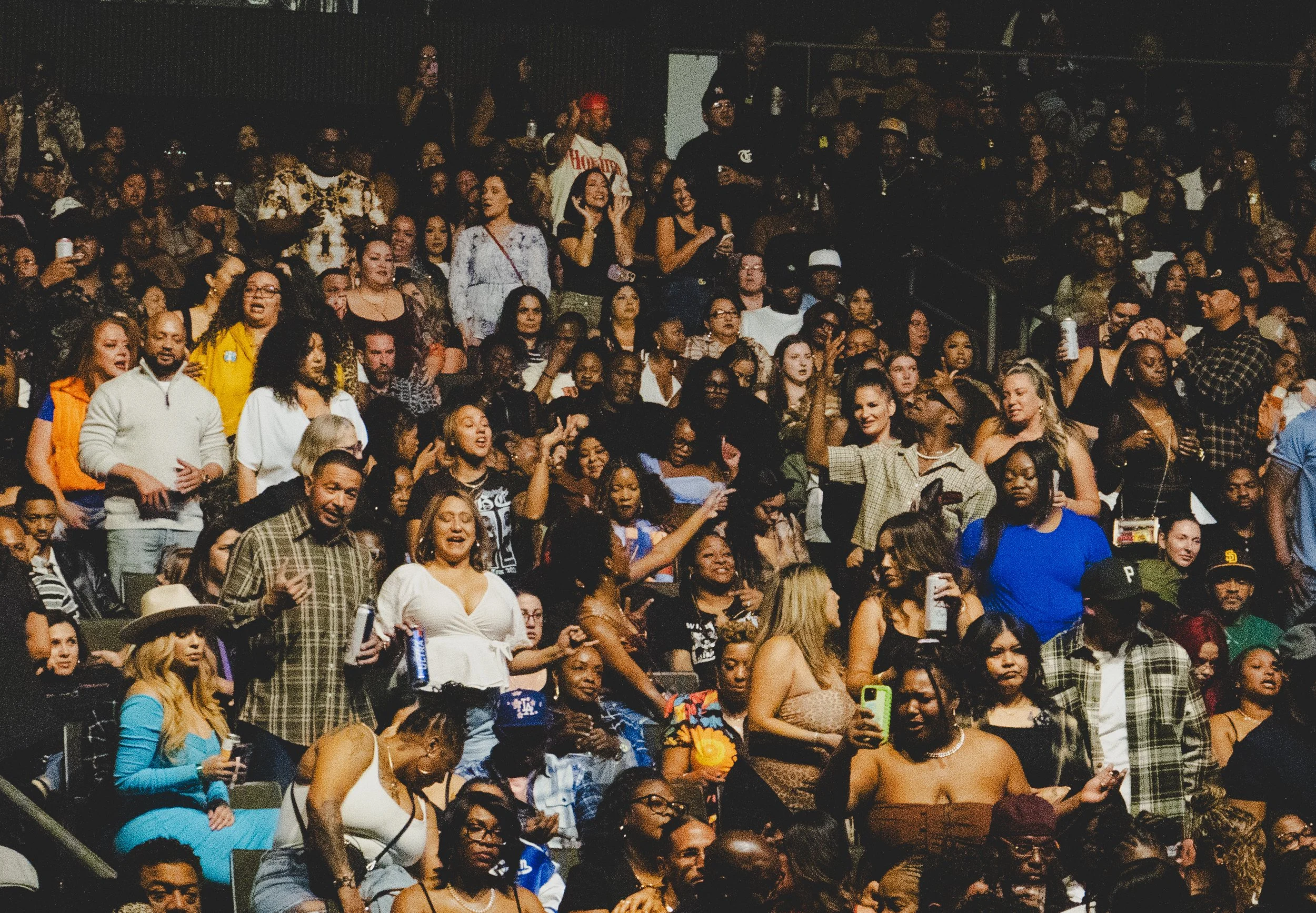 Crowd of people at a concert or event, standing and seated, enjoying music or entertainment in a dark indoor venue.