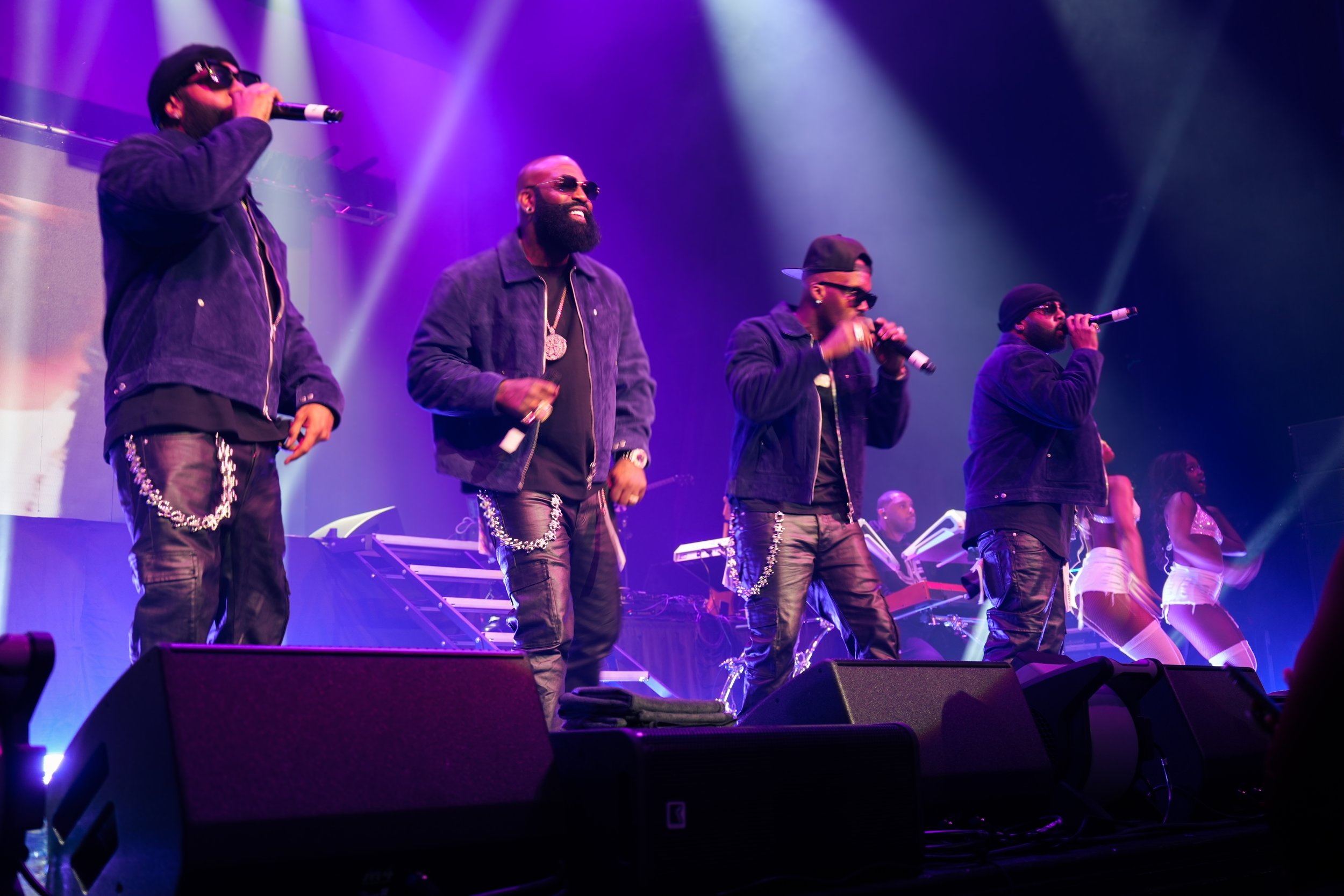 Jagged Edge performing on stage singing into microphones during a concert, with two female dancers in the background.