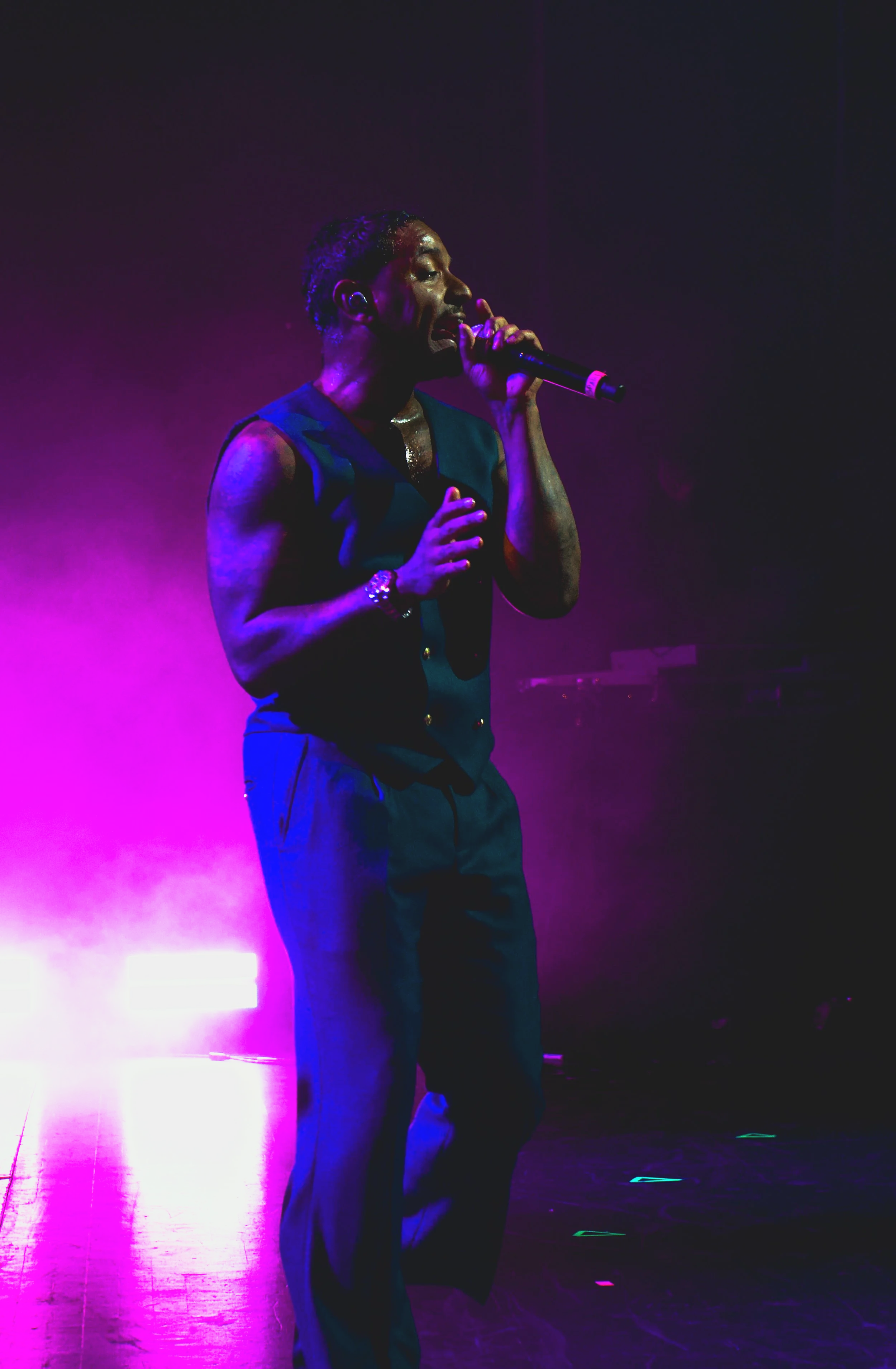 A male singer performing on stage, holding a microphone with purple and pink stage lighting.