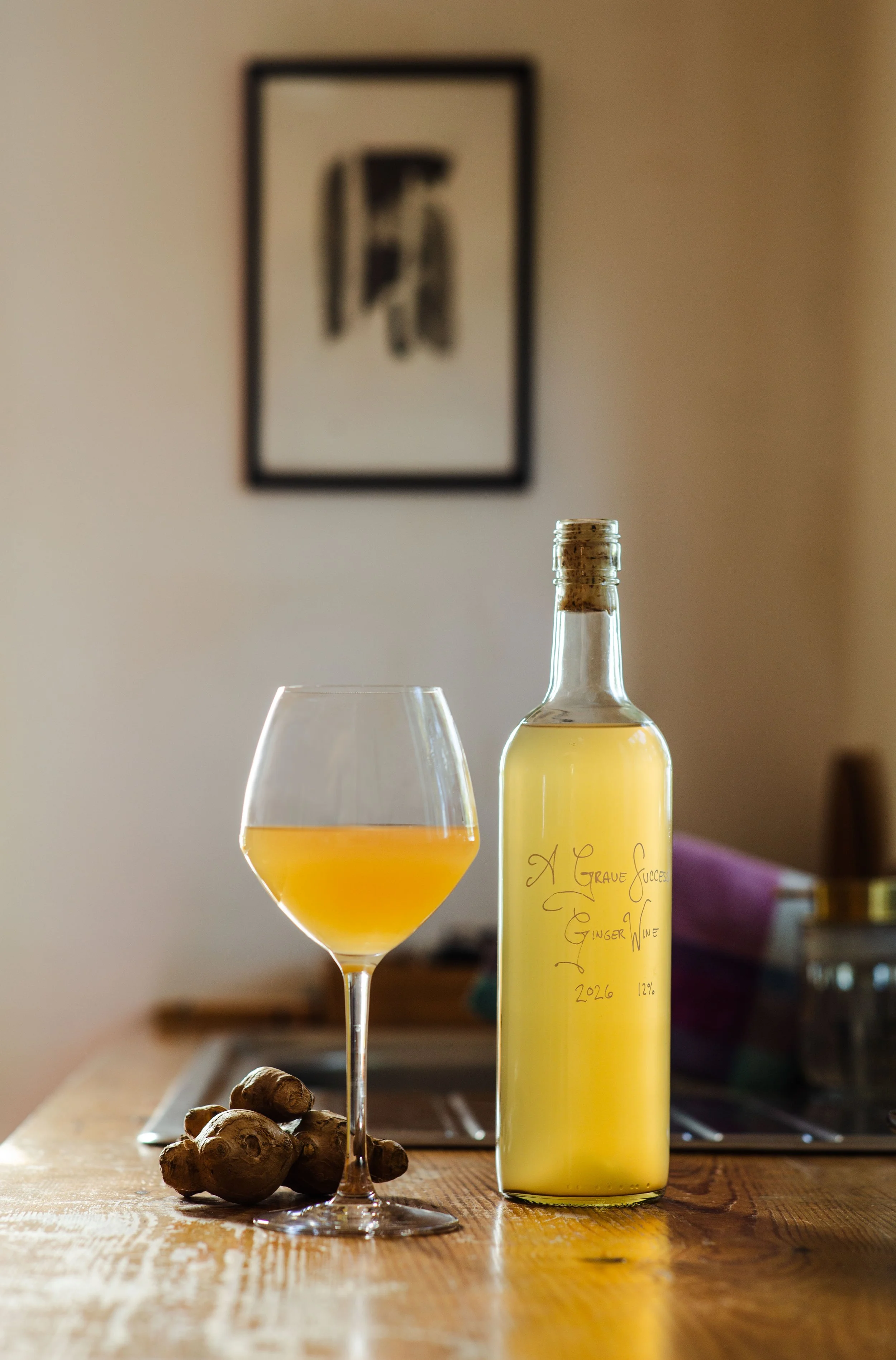 A glass of ginger wine sits next to a bottle of ginger wine on a wooden countertop