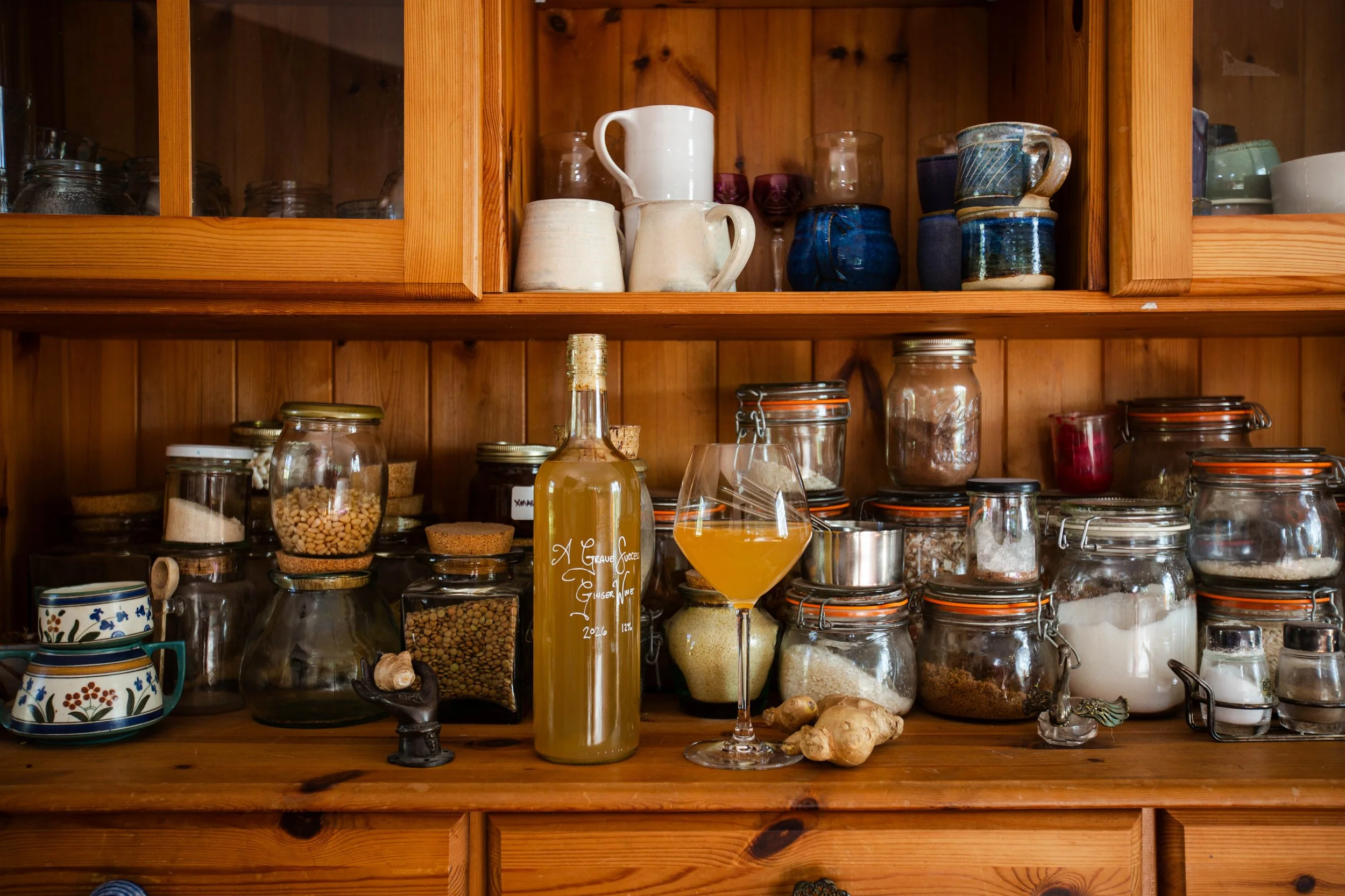 A bottle of ginger wine and a glass of ginger wine sit within a spice cabinet