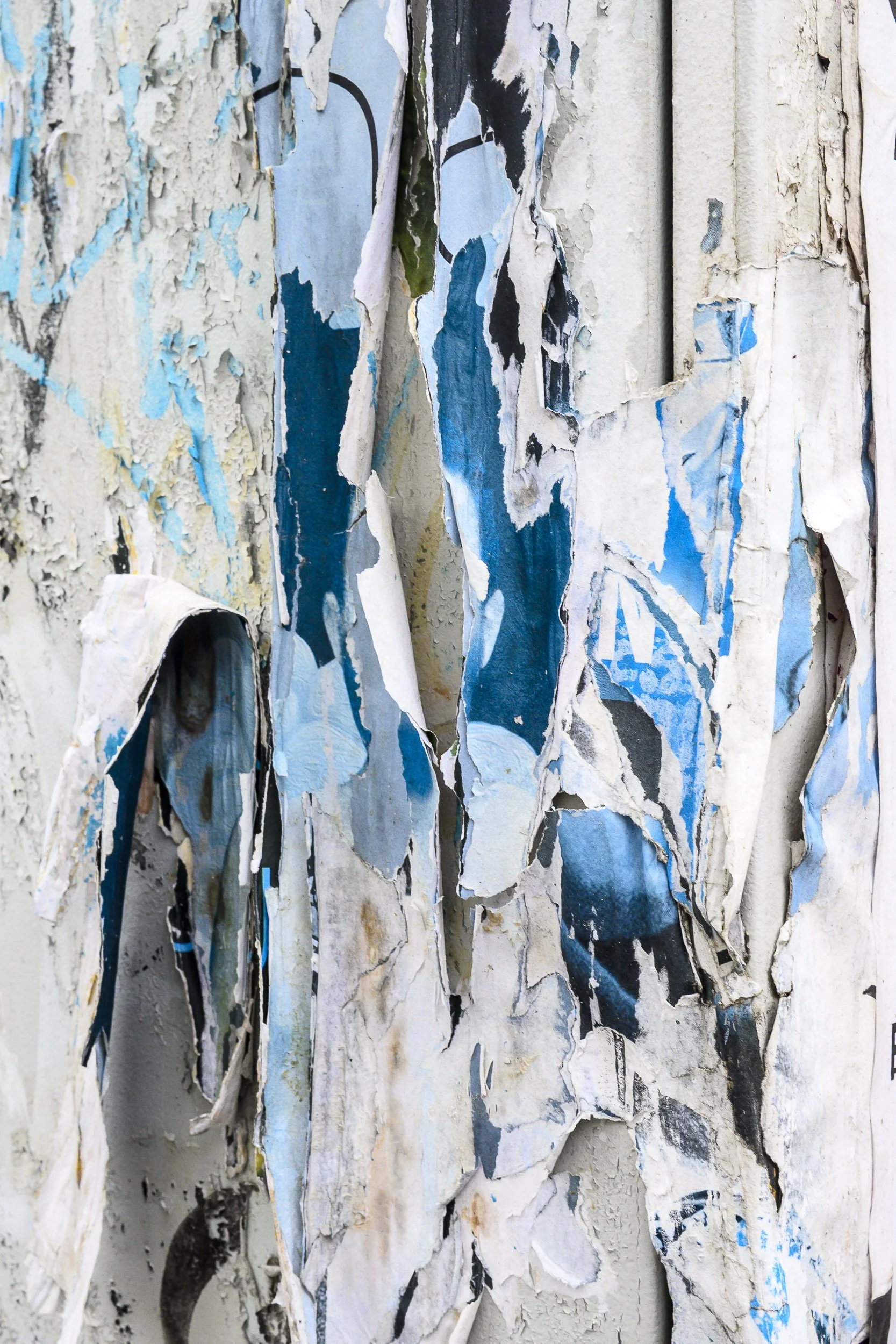 Pared con papel tapiz rasgado y desgastado, con pedazos de papel en diferentes colores, principalmente en tonos azules, blancos y negros.