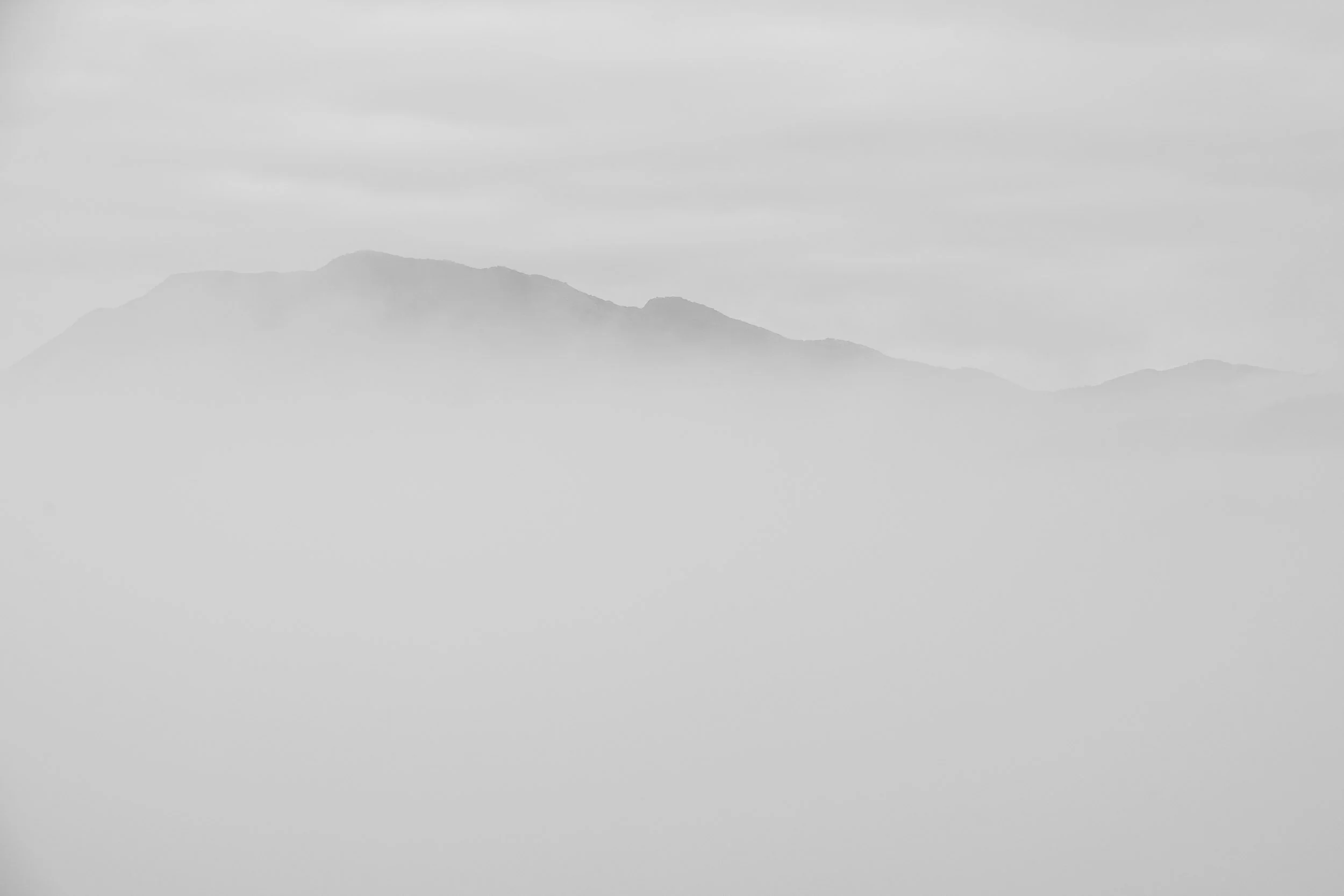 Montaña cubierta de niebla con cielo nublado, en tonos de gris.