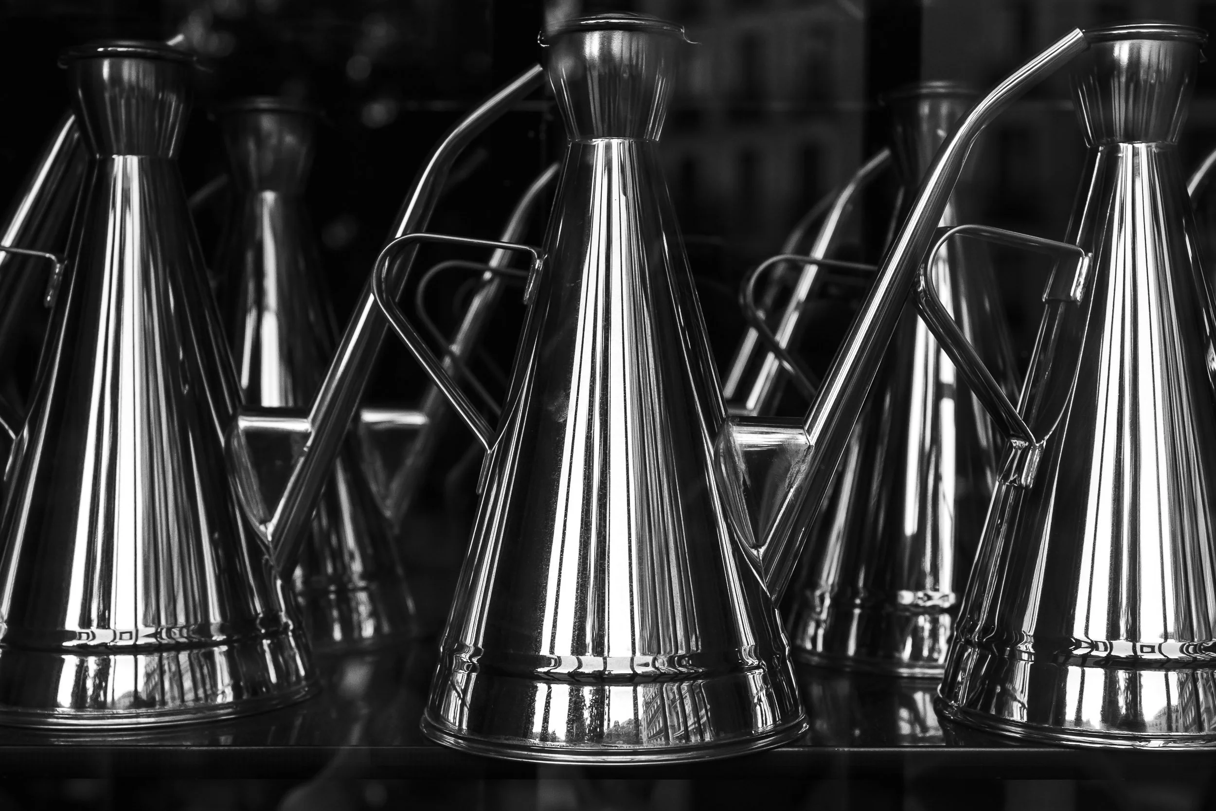 Varios embudos de metal en una estantería, en color negro y blanco.