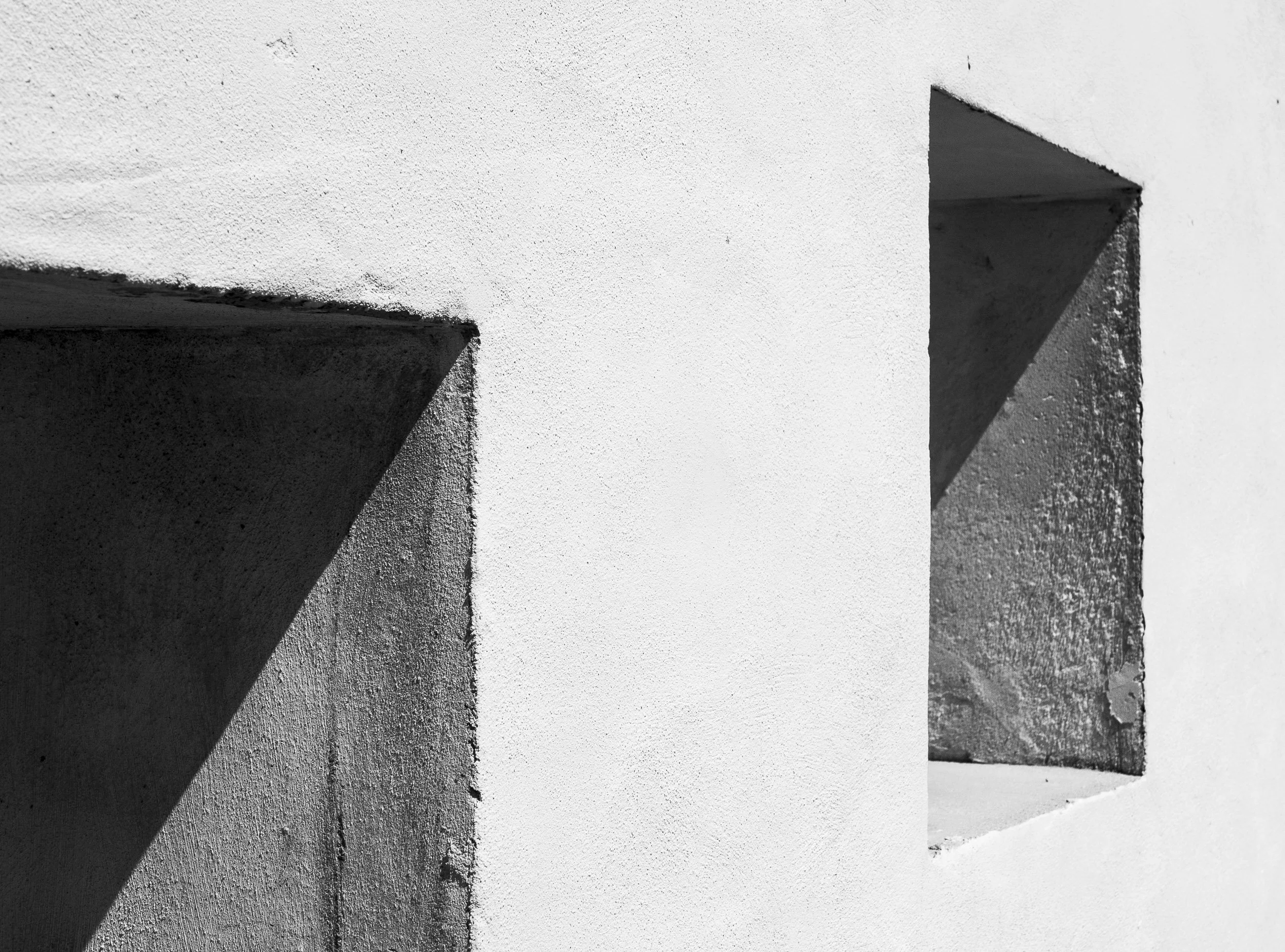 Ventanas en una pared blanca de concreto, con sombras en forma triangular en las esquinas.