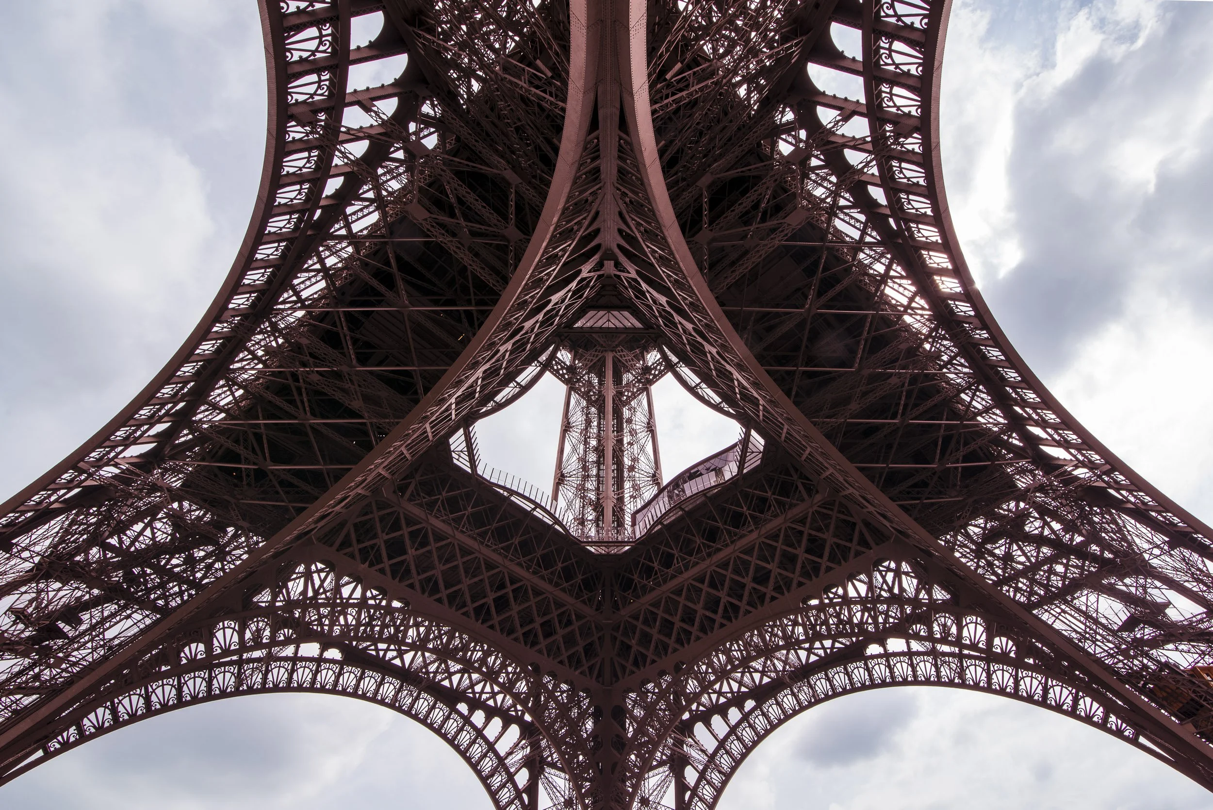 Vista desde abajo de la estructura metálica de la Torre Eiffel en París, con cielo nublado de fondo.