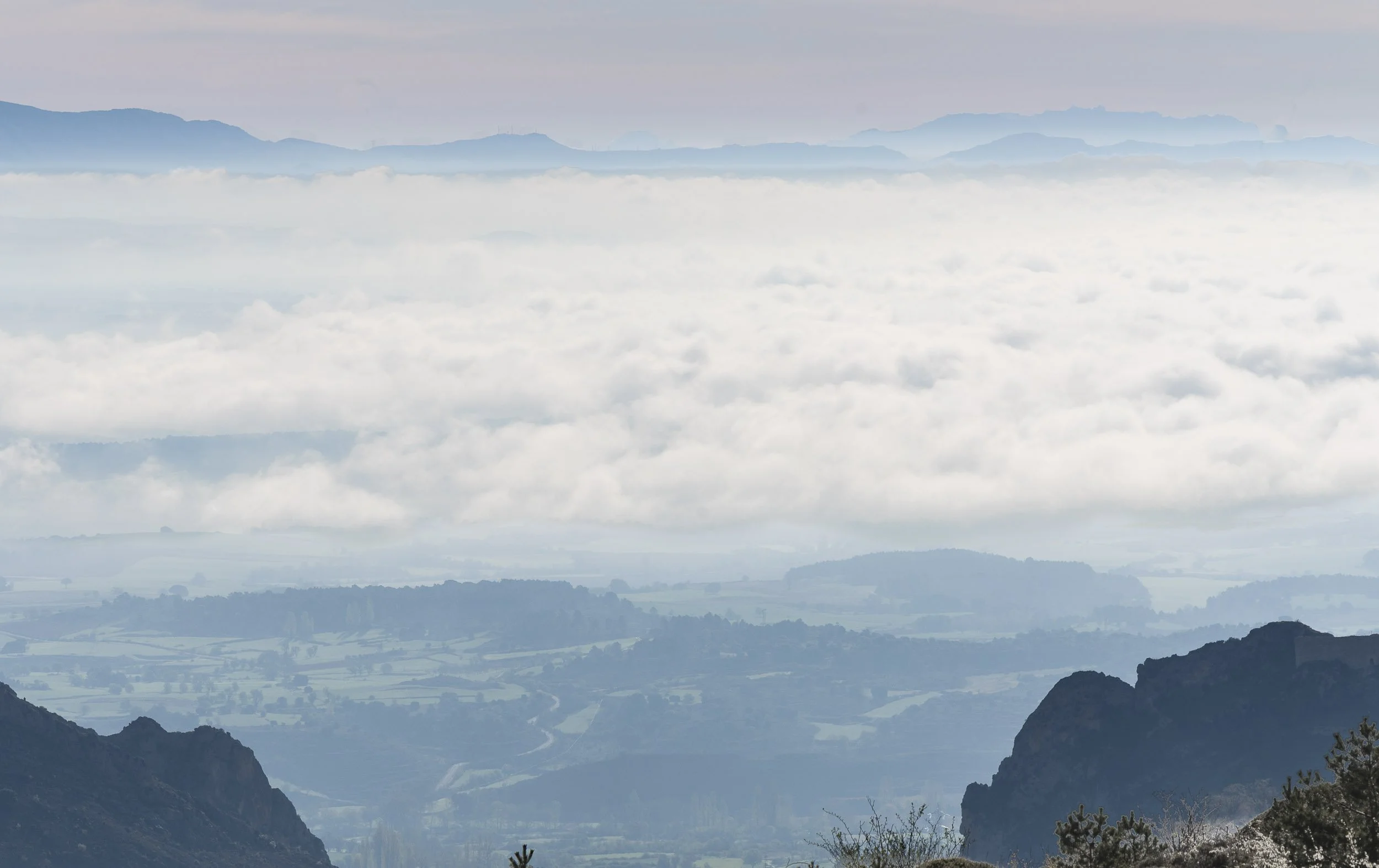 Vista de montañas y valles cubiertos de nubes y neblina, con cadenas montañosas en el fondo.