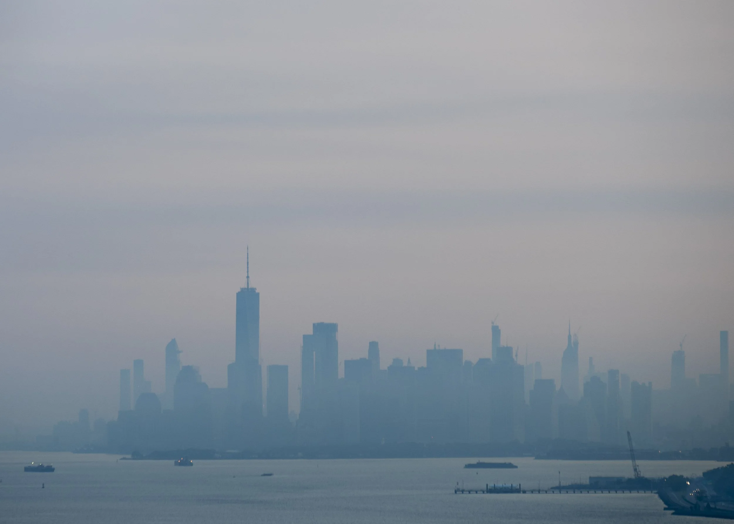 Vista del skyline de la ciudad de Nueva York con edificios altos y el río en primer plano, en un día nublado.
