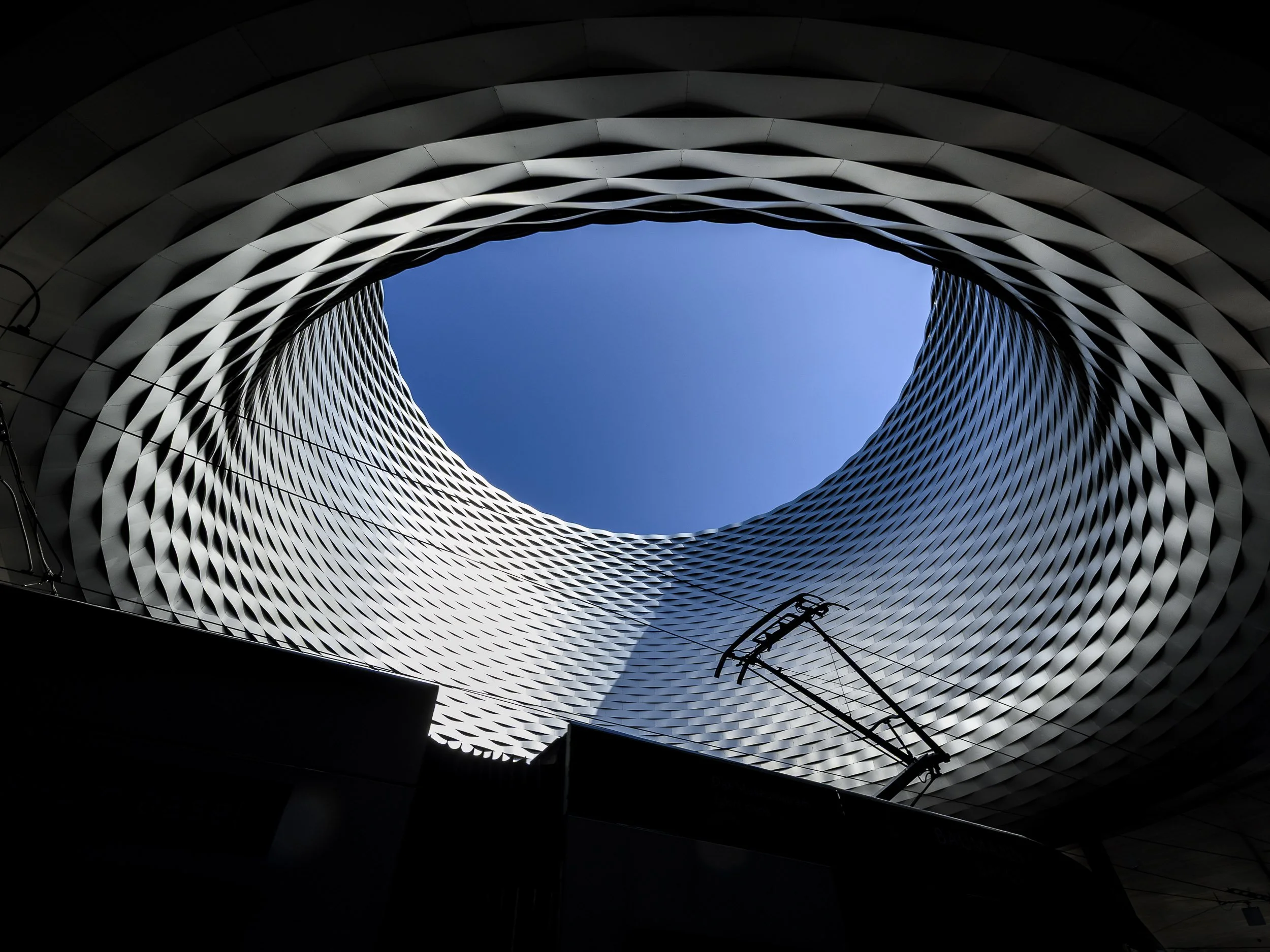 Vista desde abajo de un edificio moderno con paredes de diseño ondulado y la apertura al cielo visible en el centro.