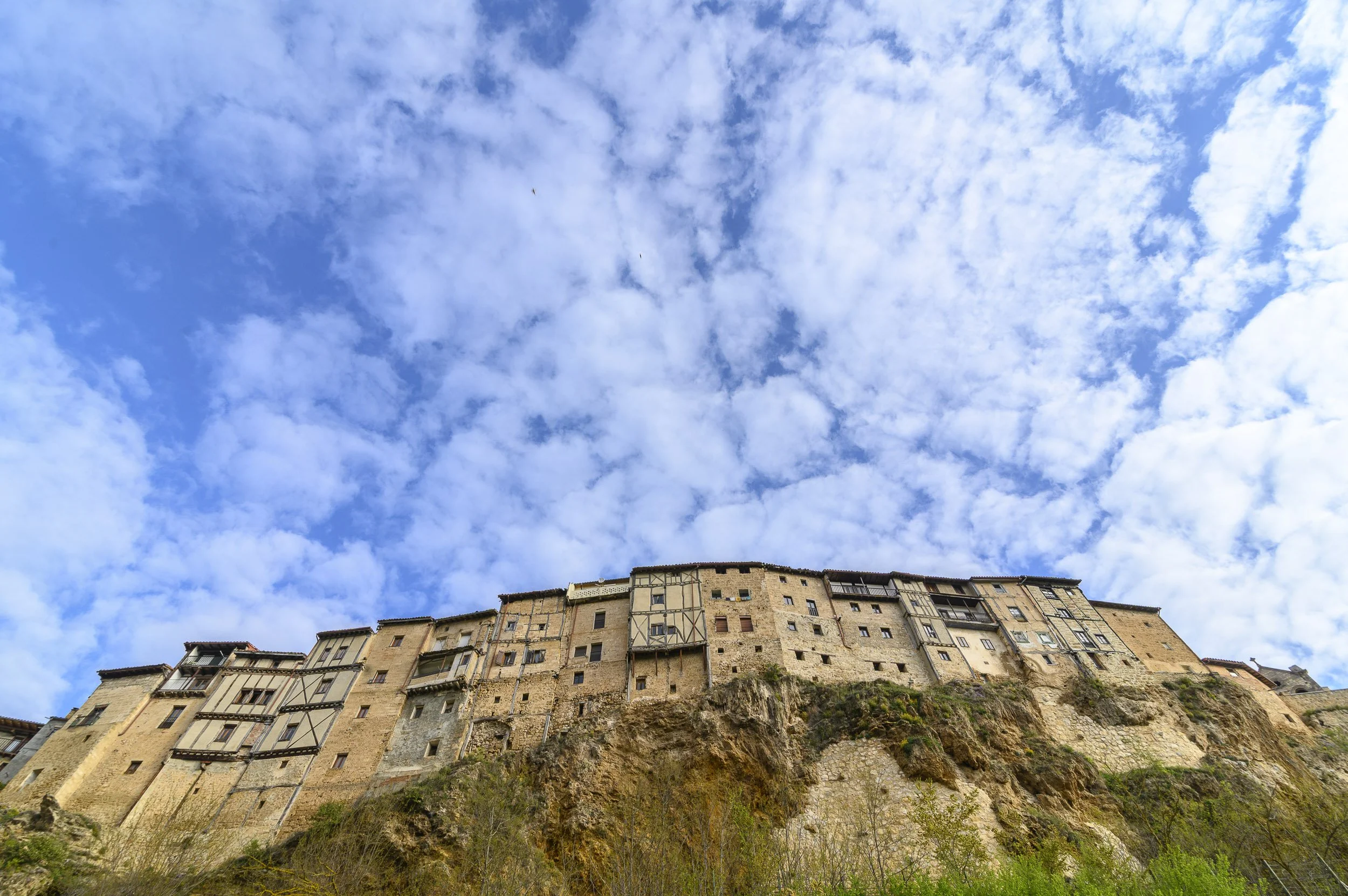 Casas antiguas construidas en la cima de un acantilado en Frías, con un cielo azul y nubes dispersas en el fondo.