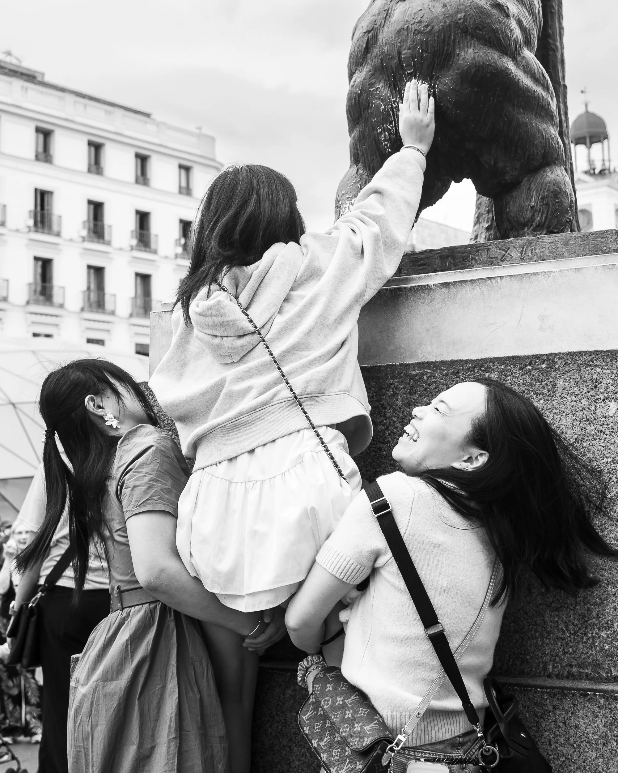 Mujer ayudando a una niña a tocar una estatua de un animal en una plaza pública
