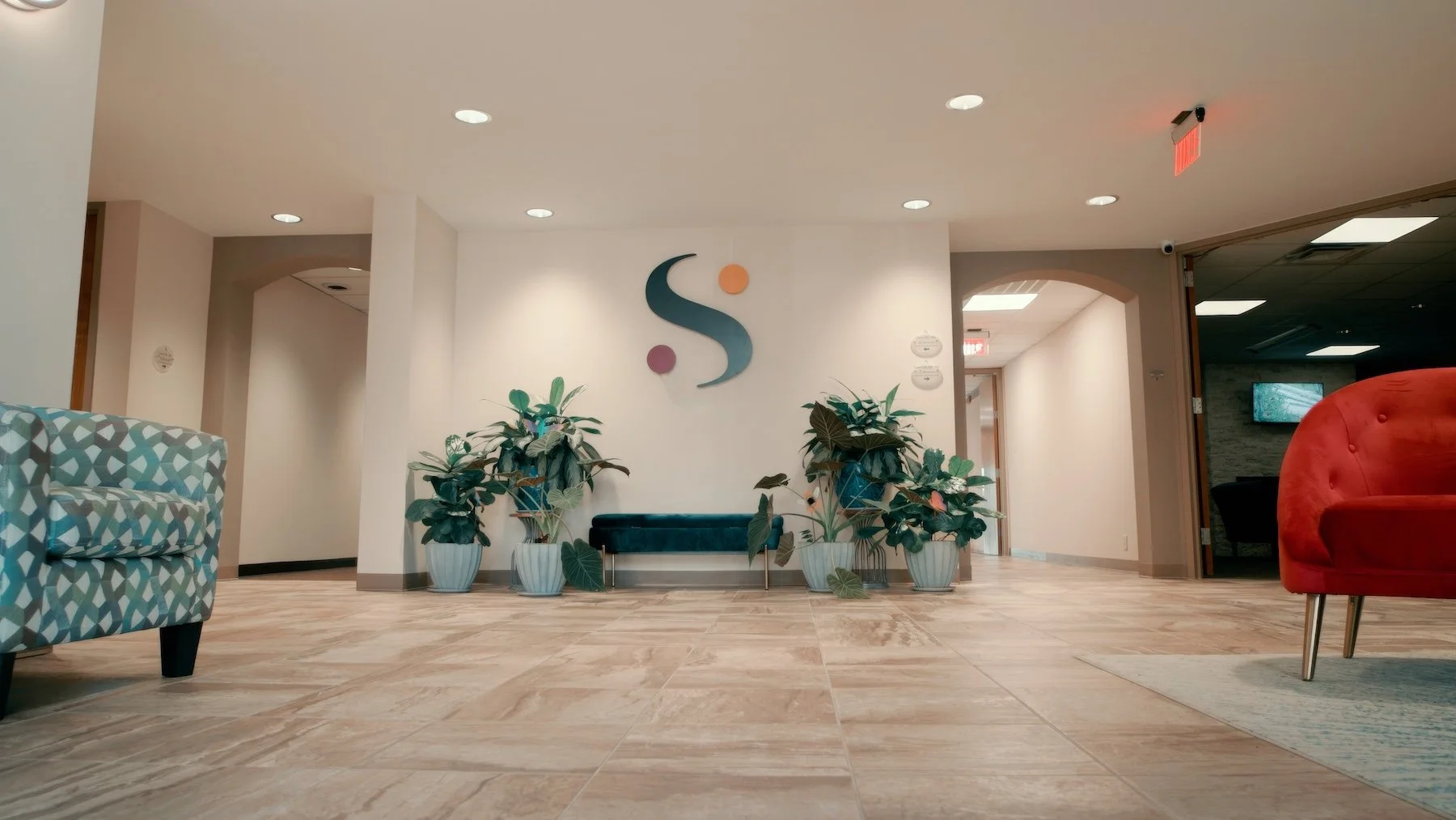 Modern hotel lobby with patterned chairs and potted plants, featuring a sign with a stylized 'S' on the wall