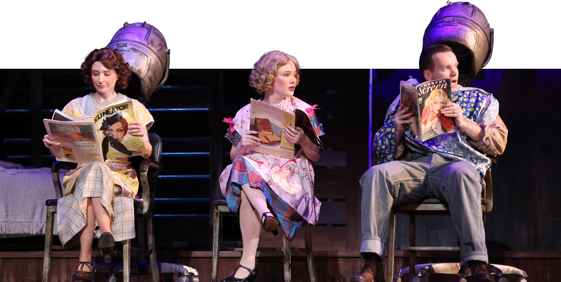 Three children sitting on stage with large studio lights behind them, reading magazines or books, dressed in vintage-style clothing.