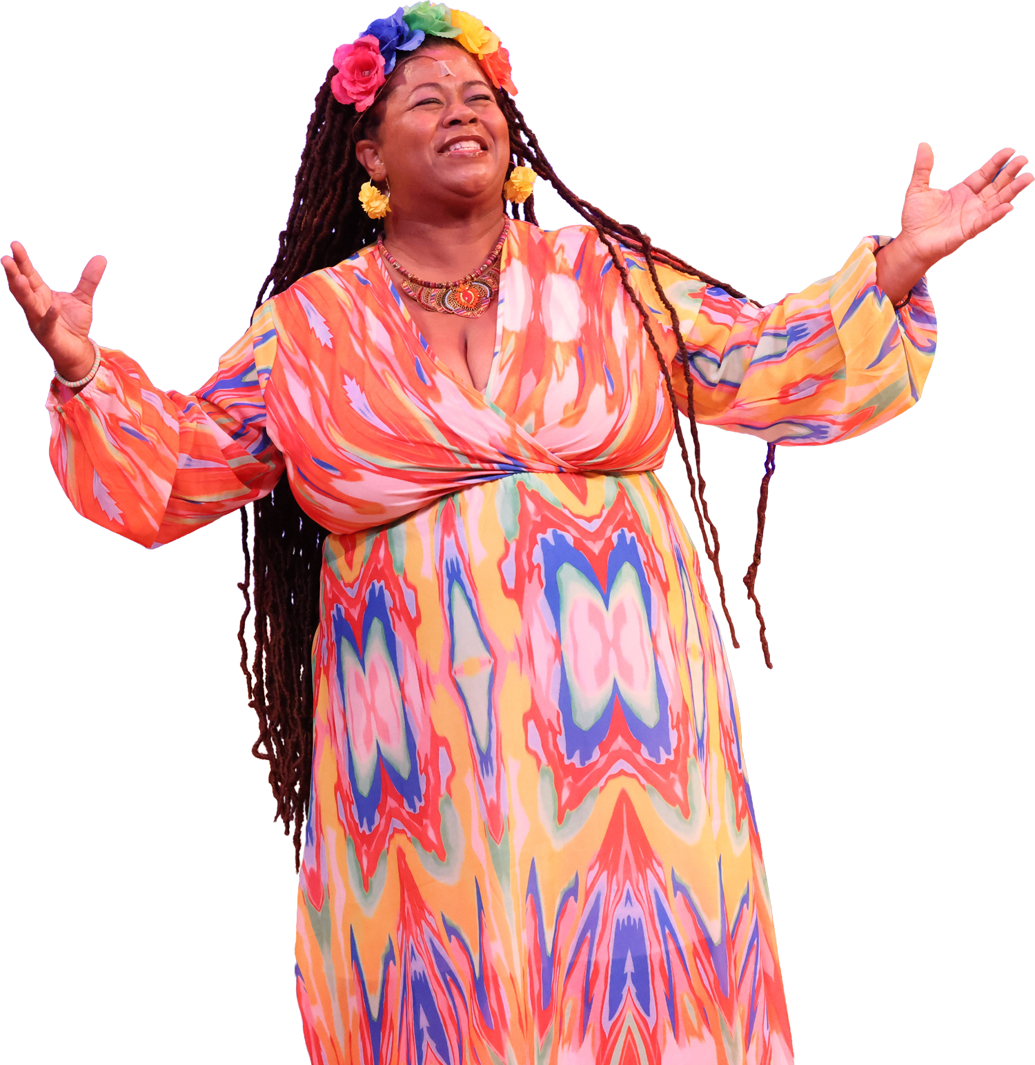 A woman with long dreadlocks wearing a colorful, patterned dress and flower crown, smiling with arms outstretched.