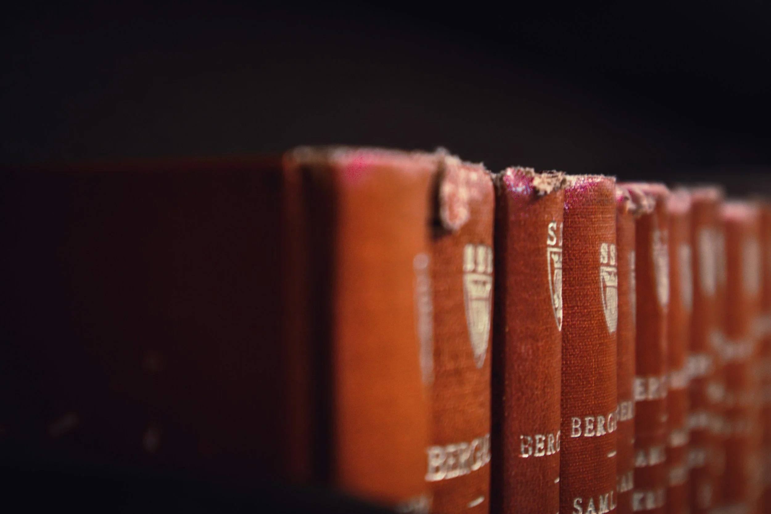 Close-up of a row of old, worn, red hardcover books on a dark background.