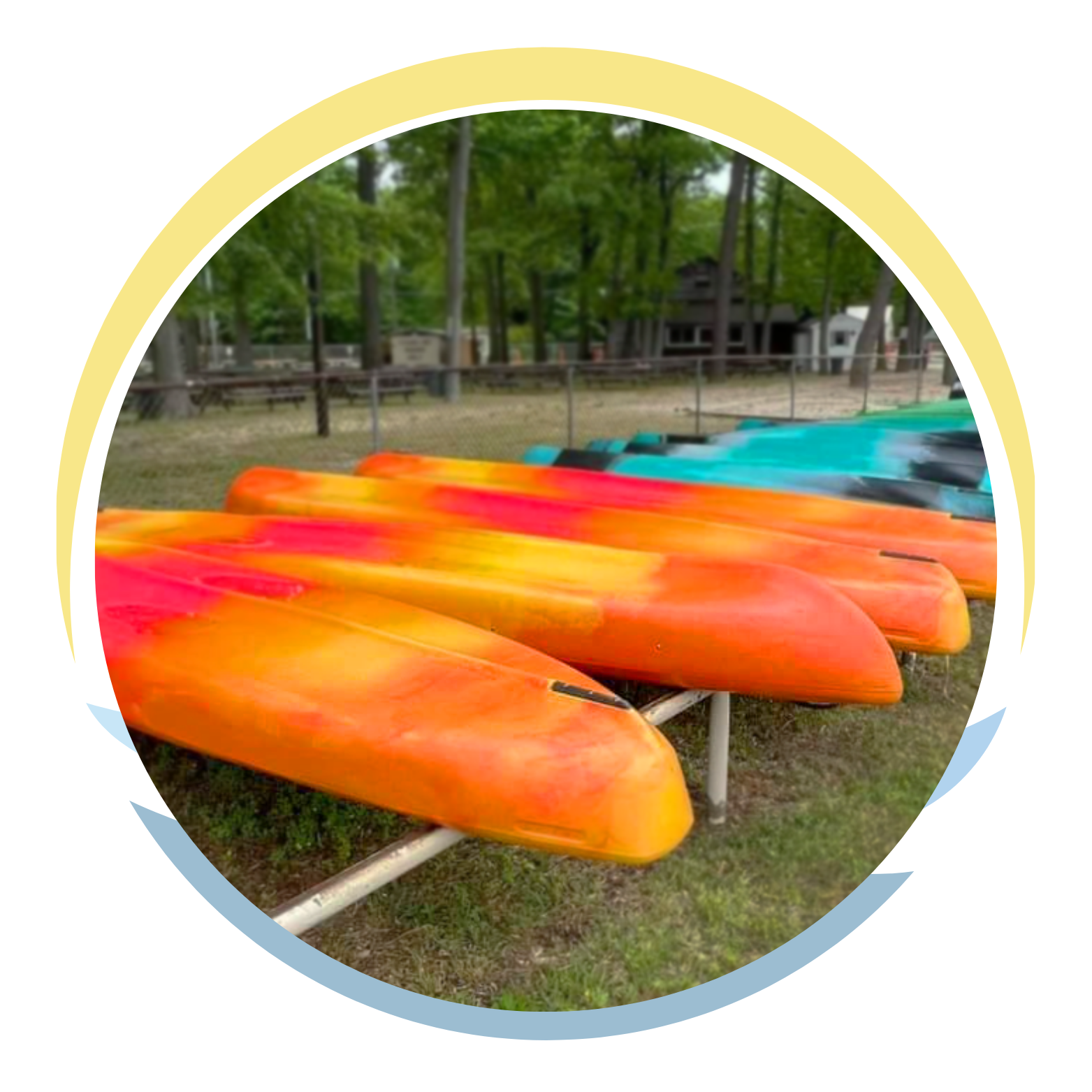Multiple colorful kayaks, primarily orange and yellow, lined up on a rack outdoors with trees and a fence in the background.