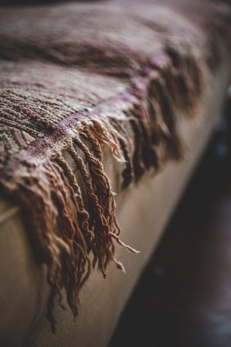 Detail view of a vintage woven fabric with frayed tassels hanging over the edge of a piece of furniture.