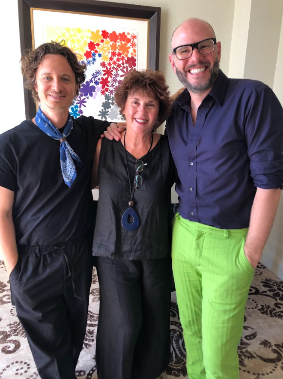 Three people standing and smiling in front of colorful flower artwork.