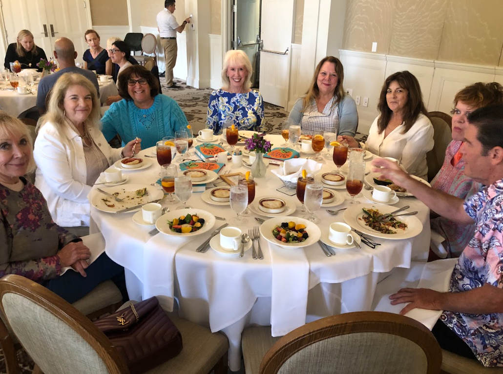 People sitting around a round dining table enjoying a meal at a social gathering, with plates of food, drinks, and decorations.