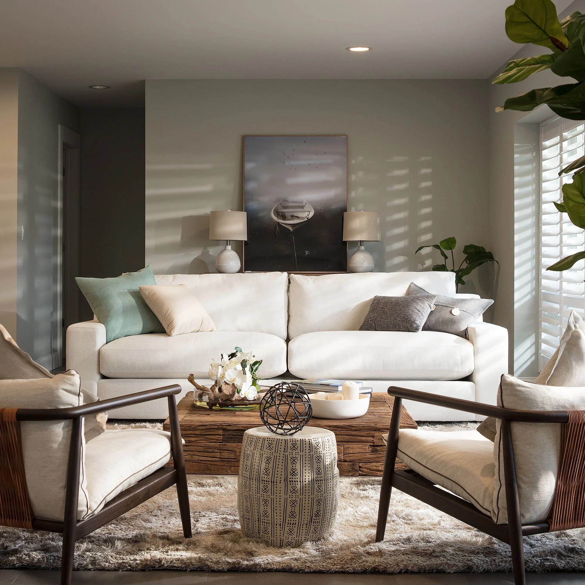 Modern coastal living room with white sofa, reclaimed wood coffee table, dark wood armchairs, and sailboat artwork in Miami, Interior Design by CURATED.