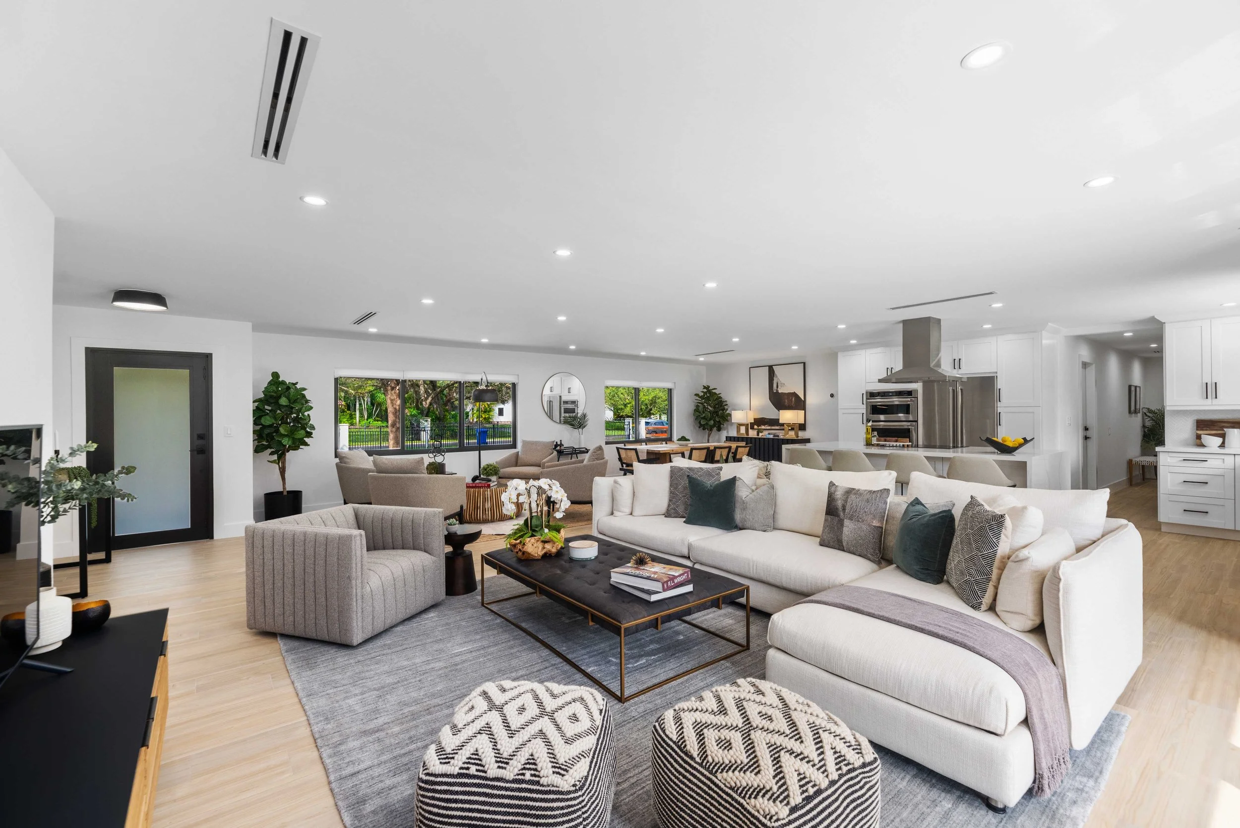 Open-concept living room with white sectional, charcoal and brass coffee table, striped swivel chair, and black-and-white patterned poufs, Interior Design by CURATED.