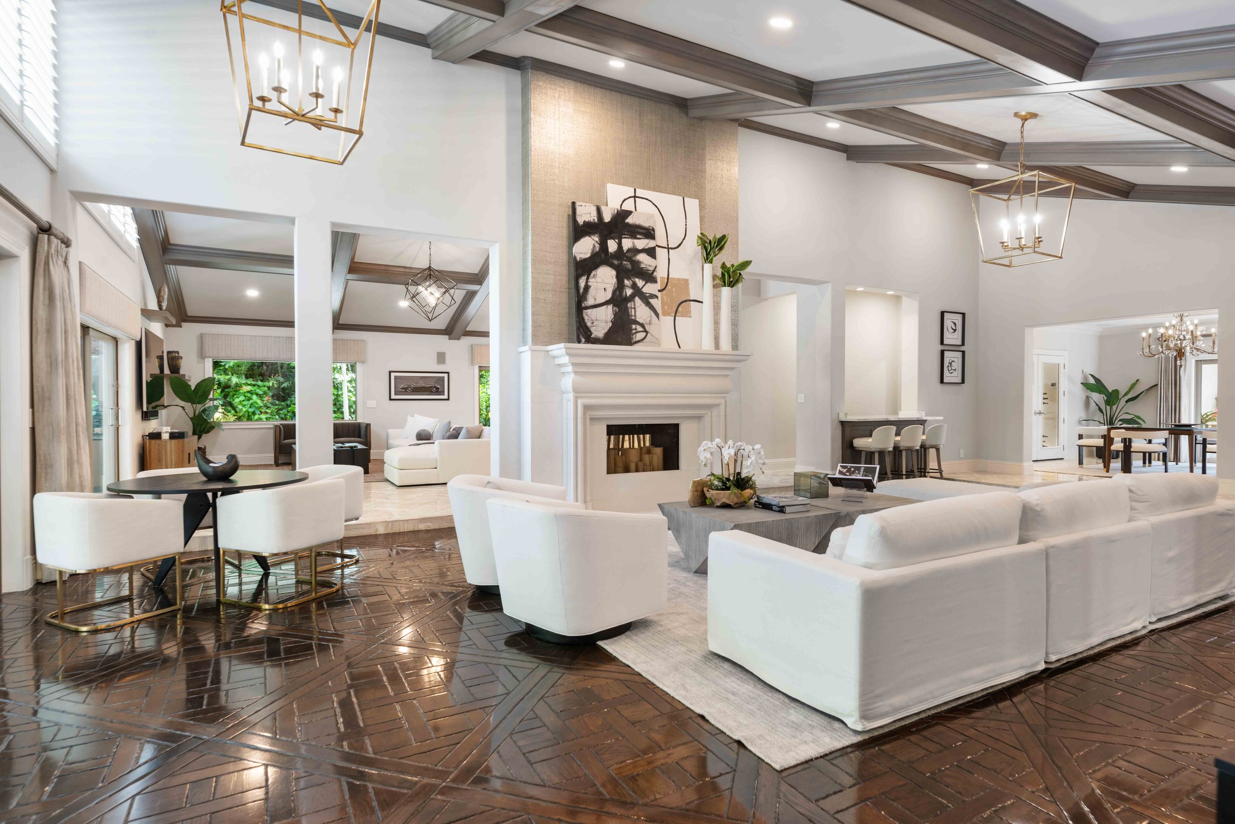 Classic living room with white slipcovered sectional, cream fireplace, brass lantern chandeliers, and dark parquet wood floors at The Sanctuary in Boca Raton, Interior Design by CURATED.