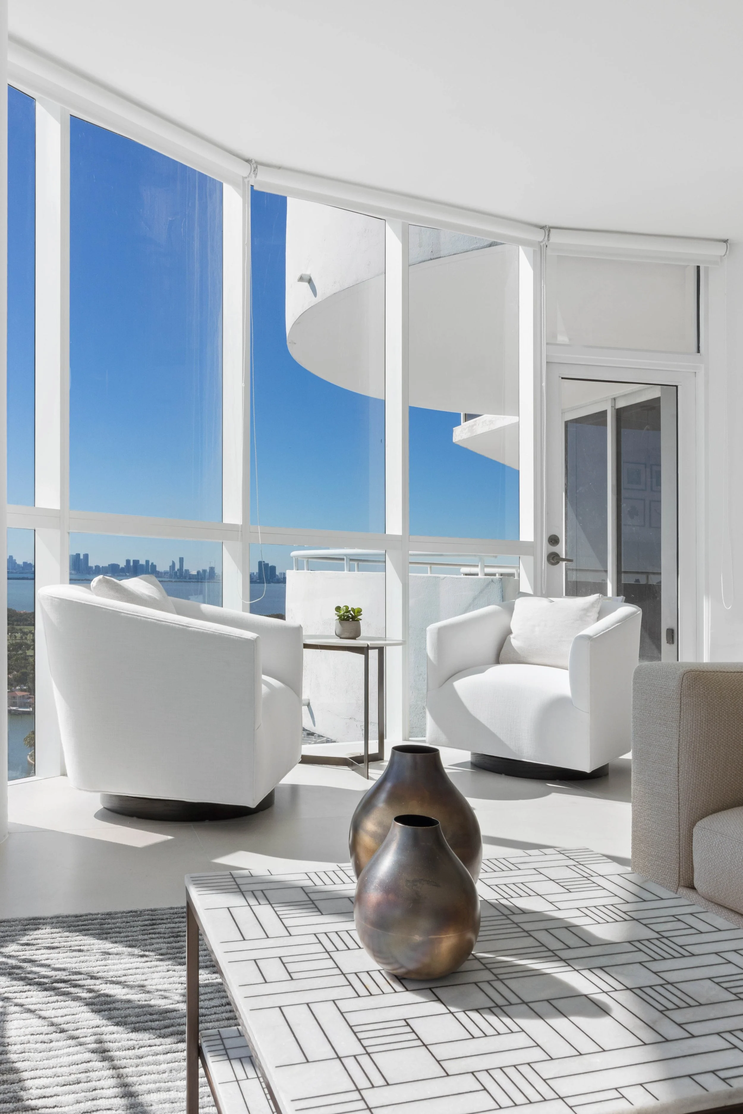 Penthouse seating area with pair of white swivel barrel chairs, slim side table, and floor-to-ceiling bay and skyline views at La Gorce Palace in Miami Beach, Interior Design by CURATED.