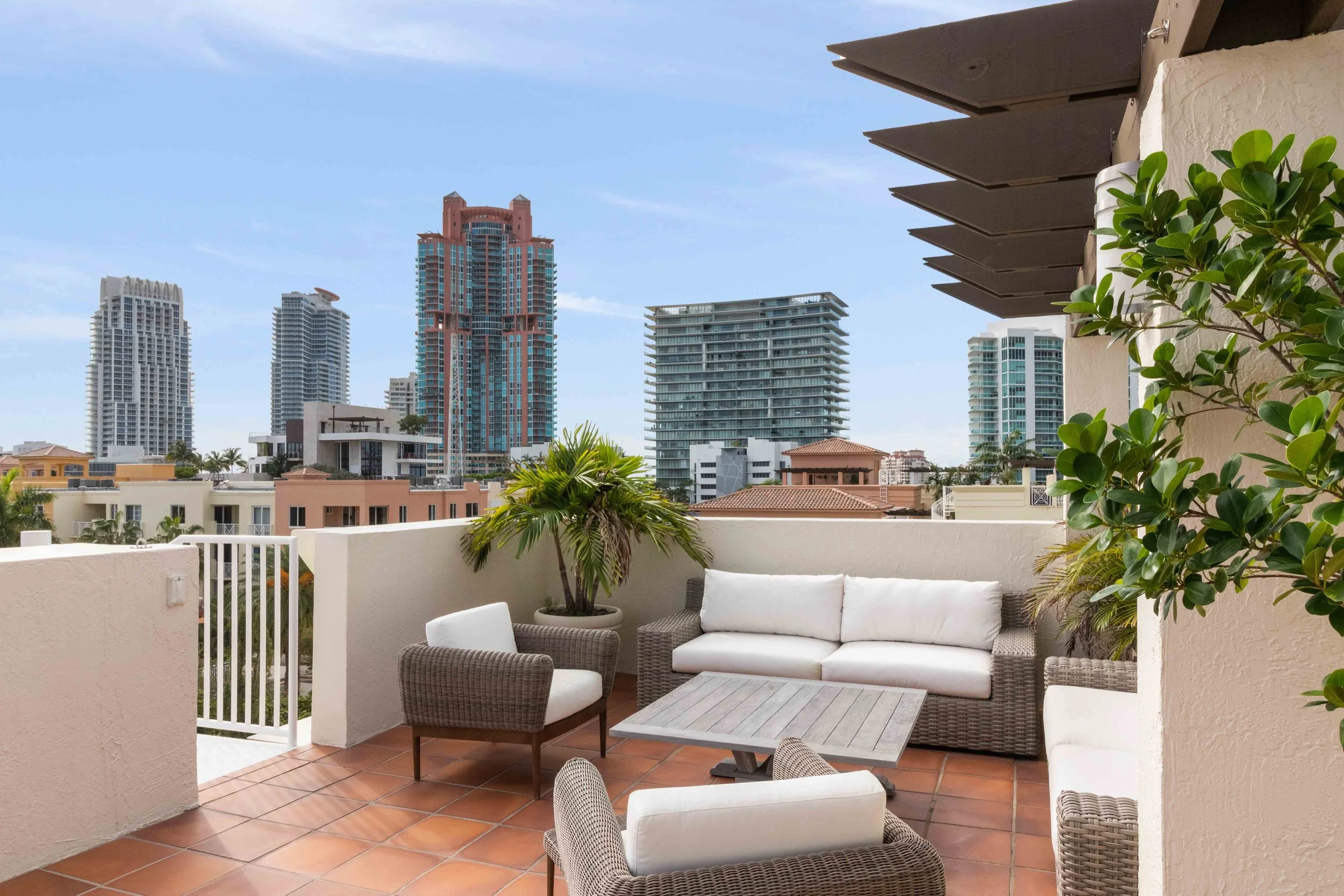 Rooftop terrace with woven wicker lounge seating, terracotta tile floors, and South Beach skyline views at The Courts in South of Fifth, Miami Beach, Interior Design by CURATED.