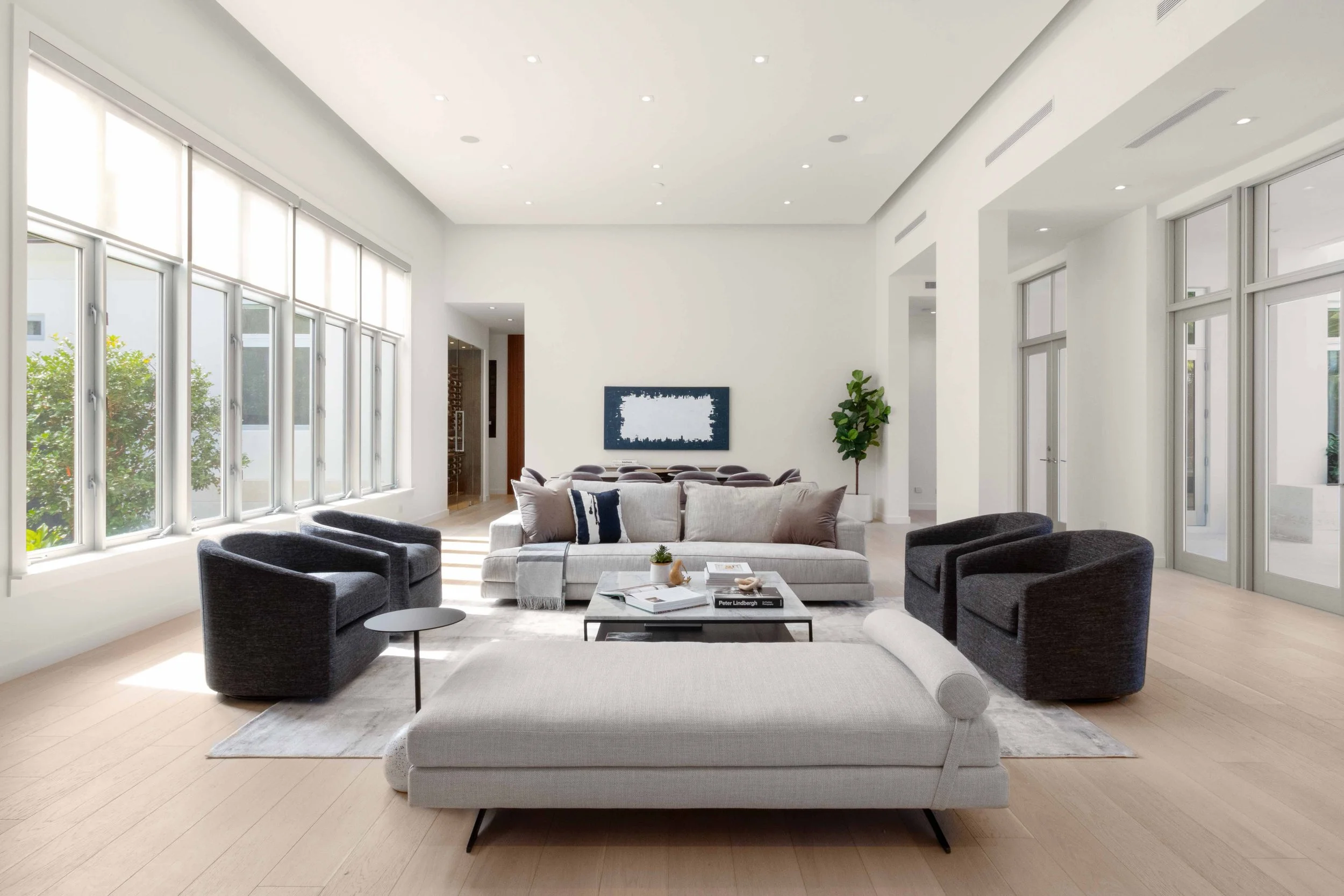 Expansive minimalist living room with light gray sofa and daybed, four charcoal swivel chairs, and wall of windows at Cocoplum in Coral Gables, Interior Design by CURATED.