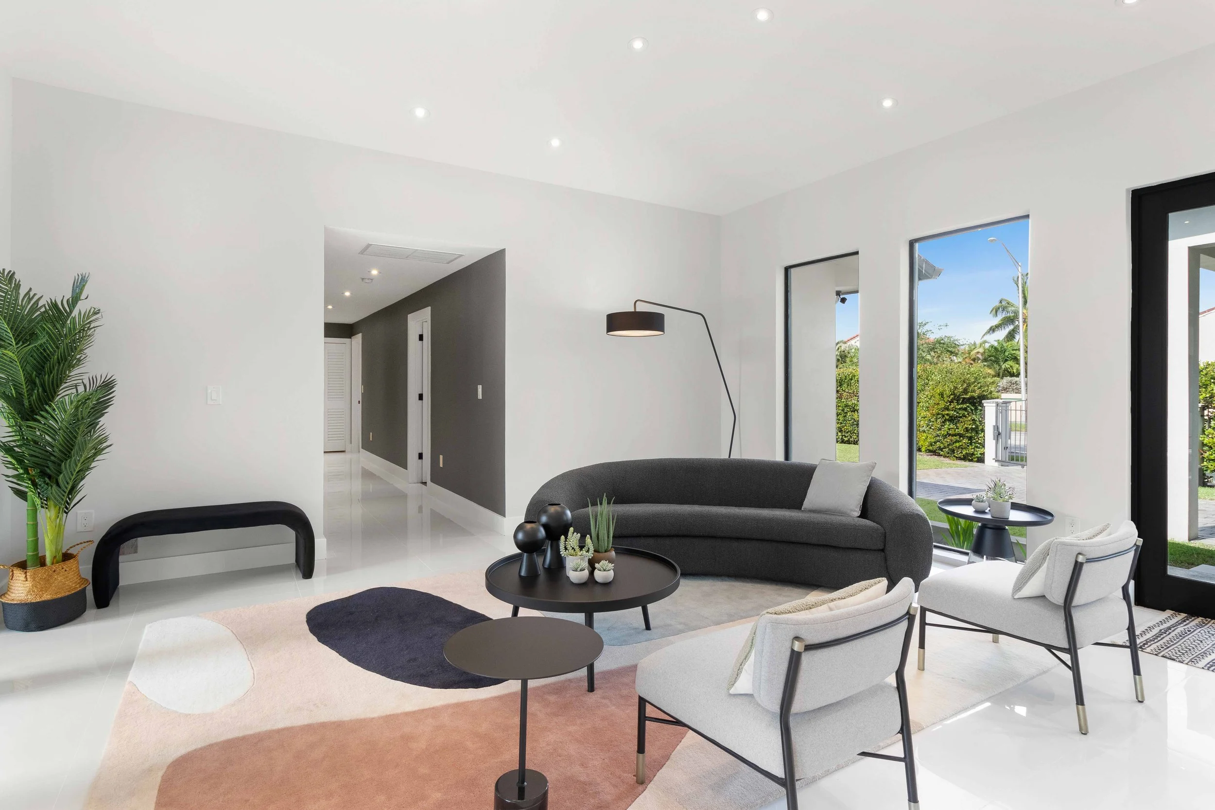 Modern living room with curved charcoal sofa, white sling armchairs, and abstract organic-shaped rug in Miami, Interior Design by CURATED.