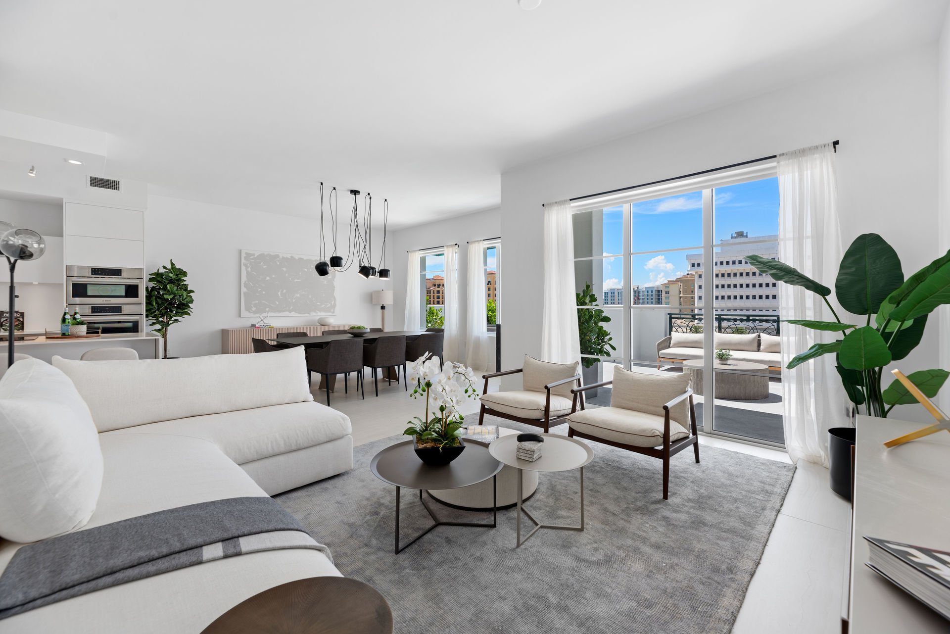 Contemporary living room with white sectional, nesting coffee tables, and cluster pendant over the dining area at Tower 155 in Boca Raton, Interior Design by CURATED.