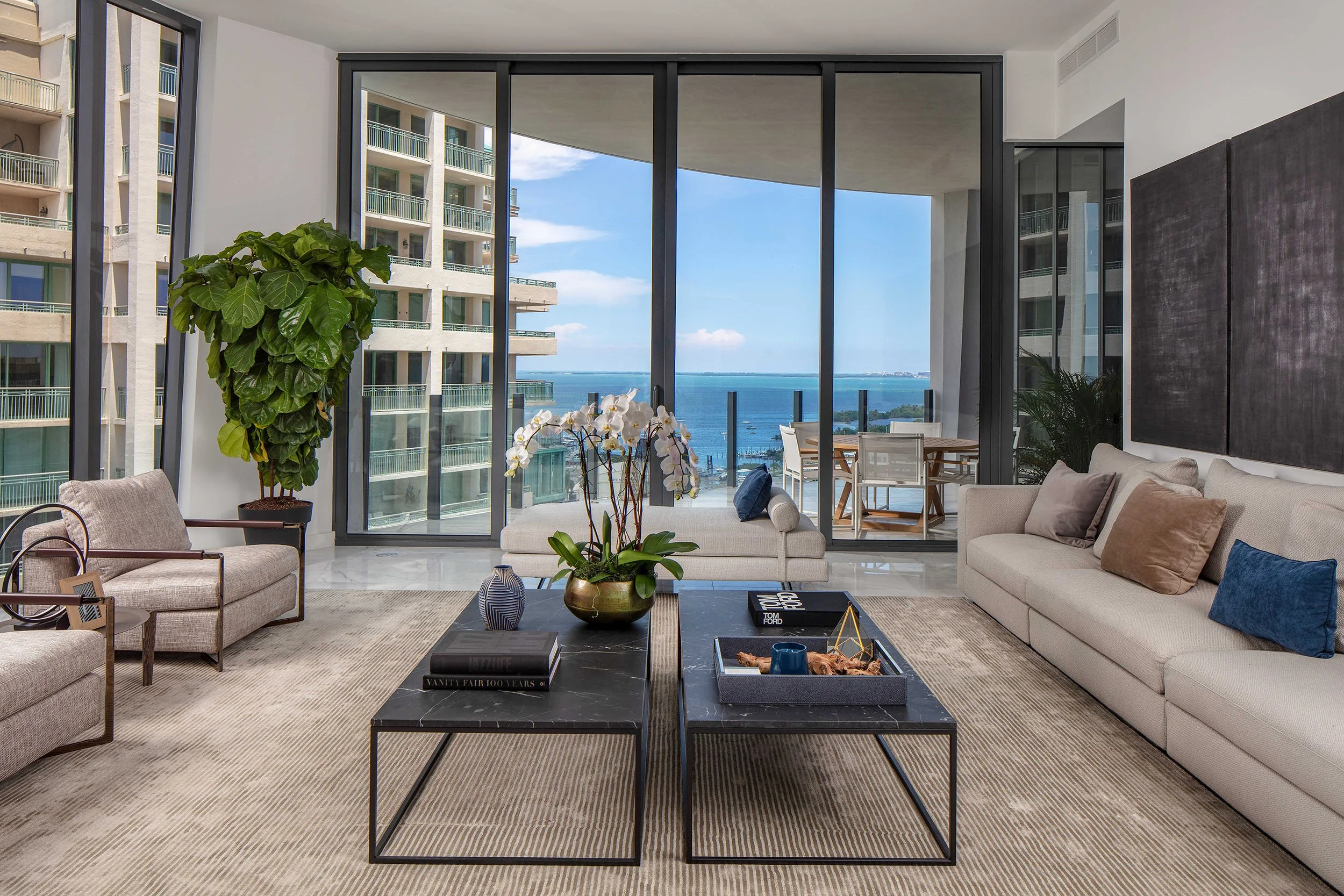 High-rise living room with beige sofa, twin dark marble coffee tables, and fiddle leaf fig overlooking the bay in Coconut Grove, Interior Design by CURATED.