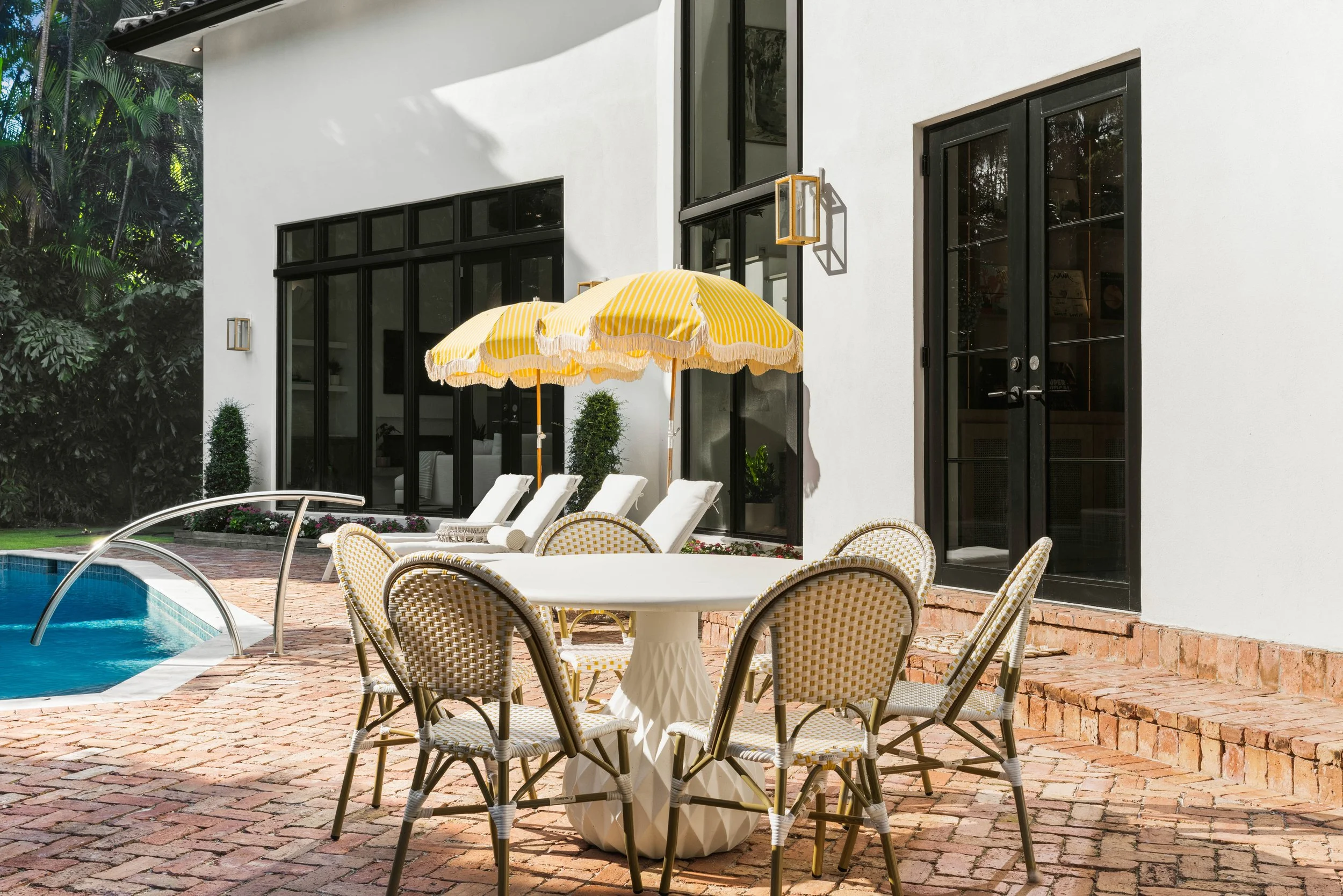 Sun loungers with bright yellow stripped umbrellas beside a outdoor dining space by the pool - Coastal Boho Estate - Coconut Grove - CURATED. Studio