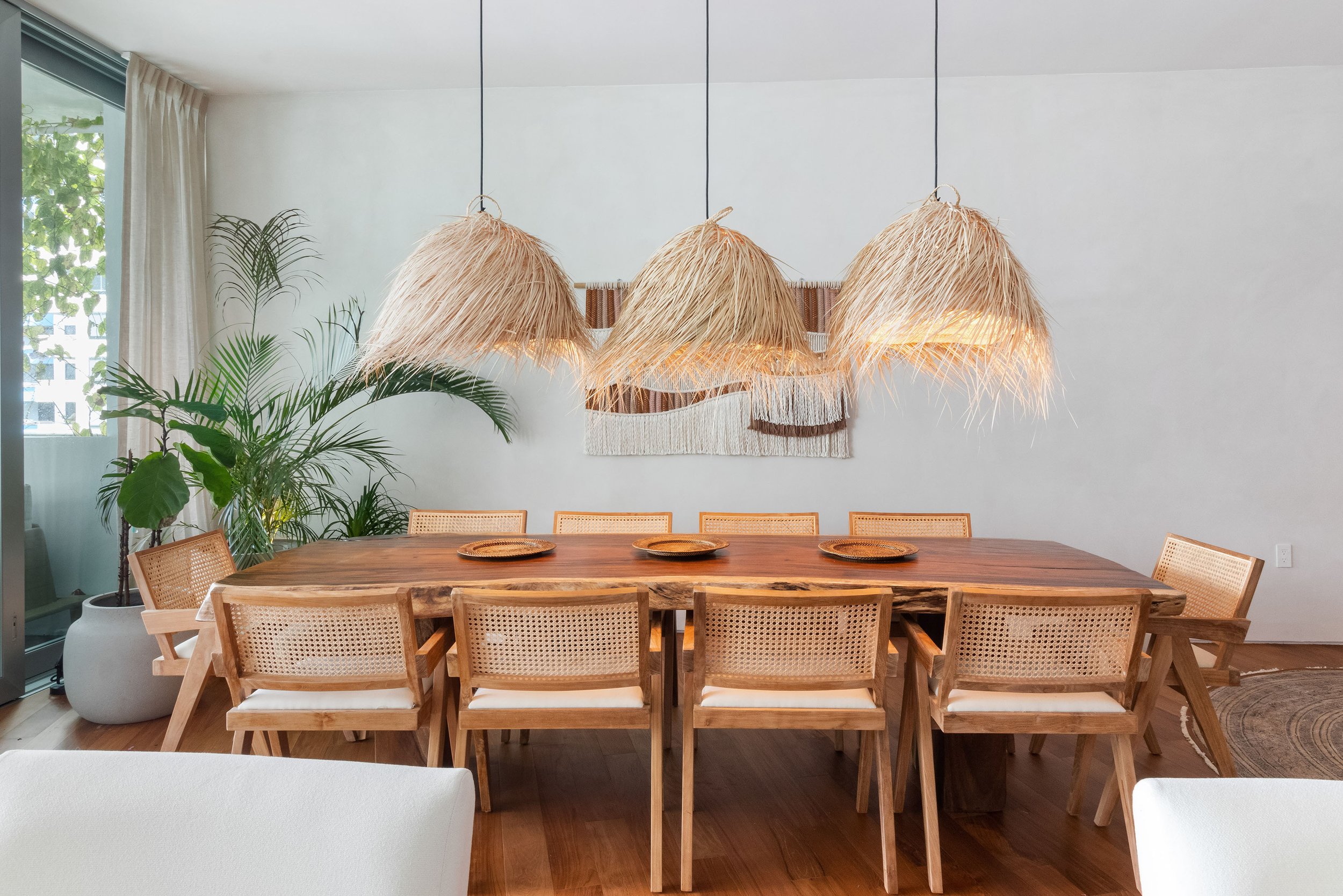 Tulum-inspired dining room with raffia pendant lights, live-edge wood table, and cane chairs at Monad Terrace in Miami Beach, Interior Design by CURATED.