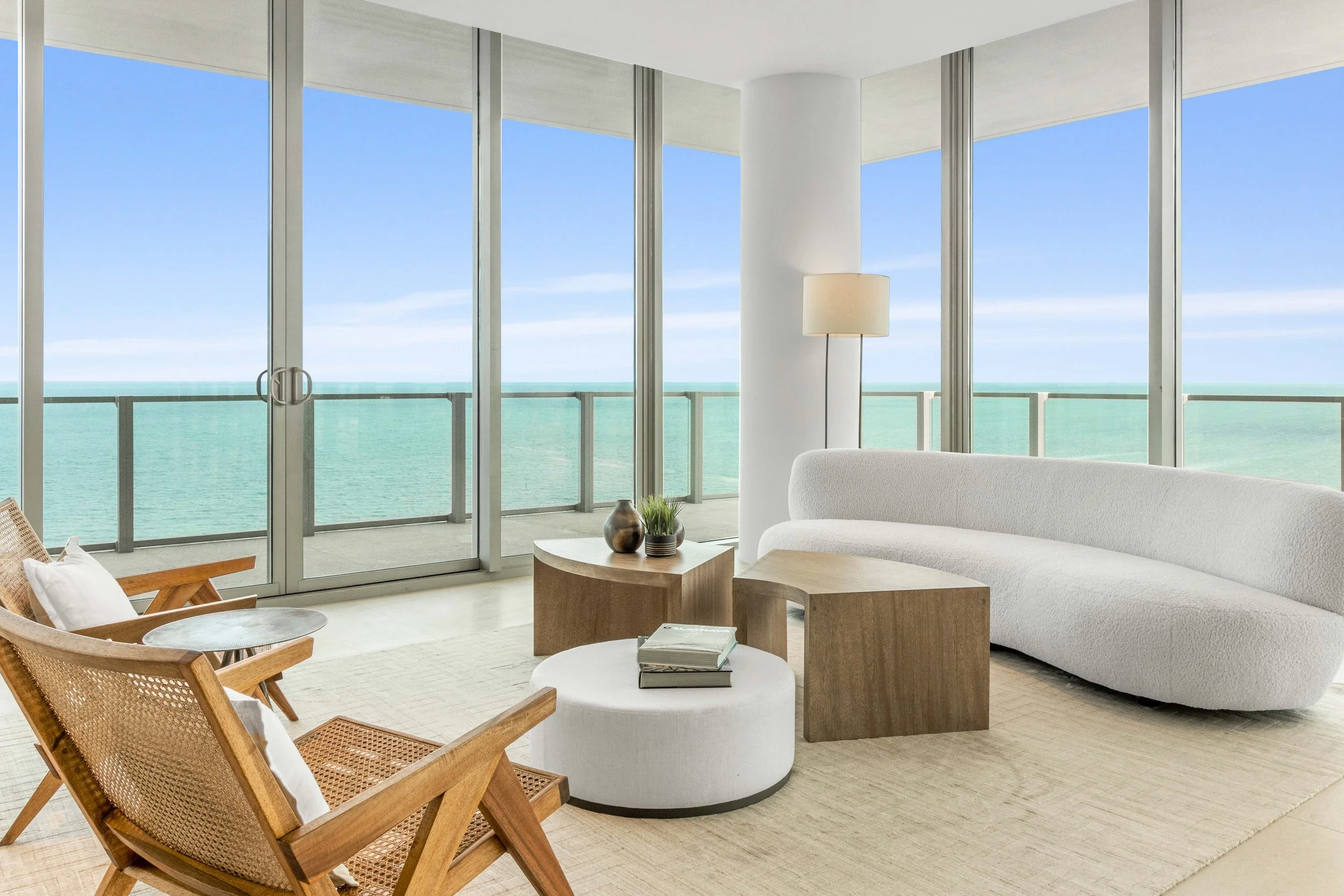 Oceanfront penthouse living room with curved white bouclé sofa, nesting wood coffee tables, and cane lounge chairs in Key Biscayne, Interior Design by CURATED.