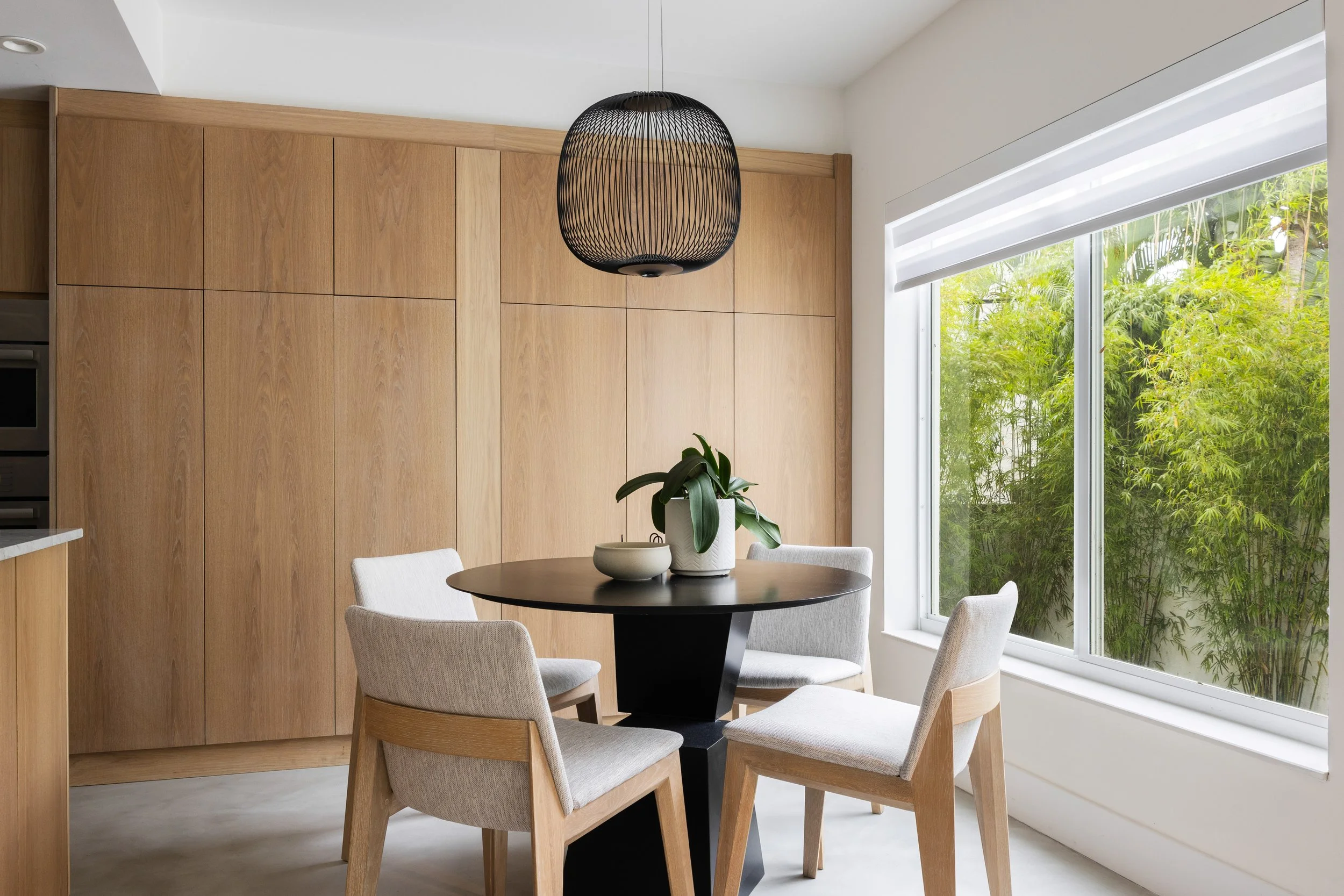 Dining space overlooking a bamboo garden adorned with warm wood cabinets - Modernized Brutalist Architecture - Coconut Grove - CURATED. Studio