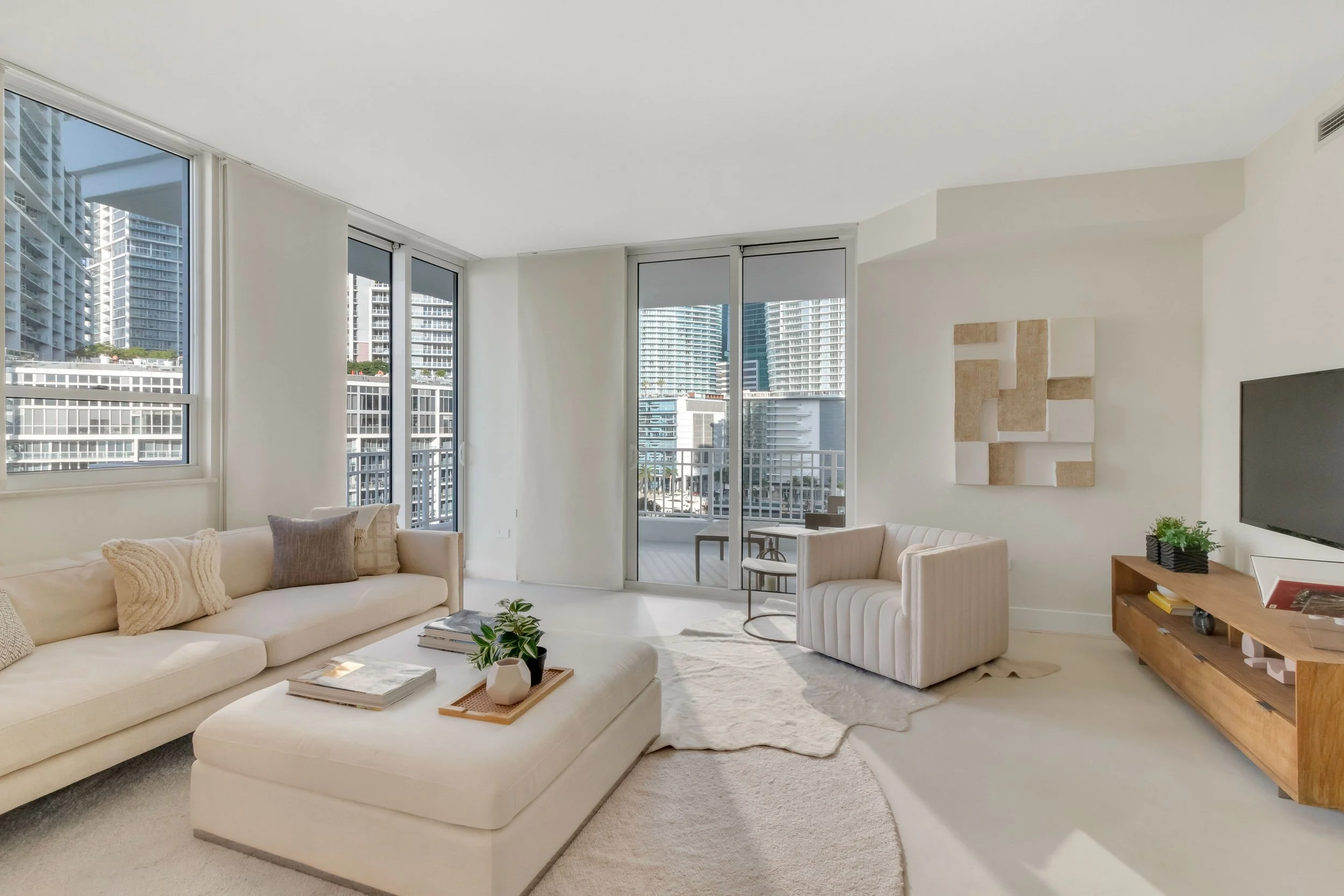 Scandinavian-inspired living room with cream sofa, upholstered ottoman, channel-tufted armchair, and light wood media console at Courts Brickell Key in Miami, Interior Design by CURATED.