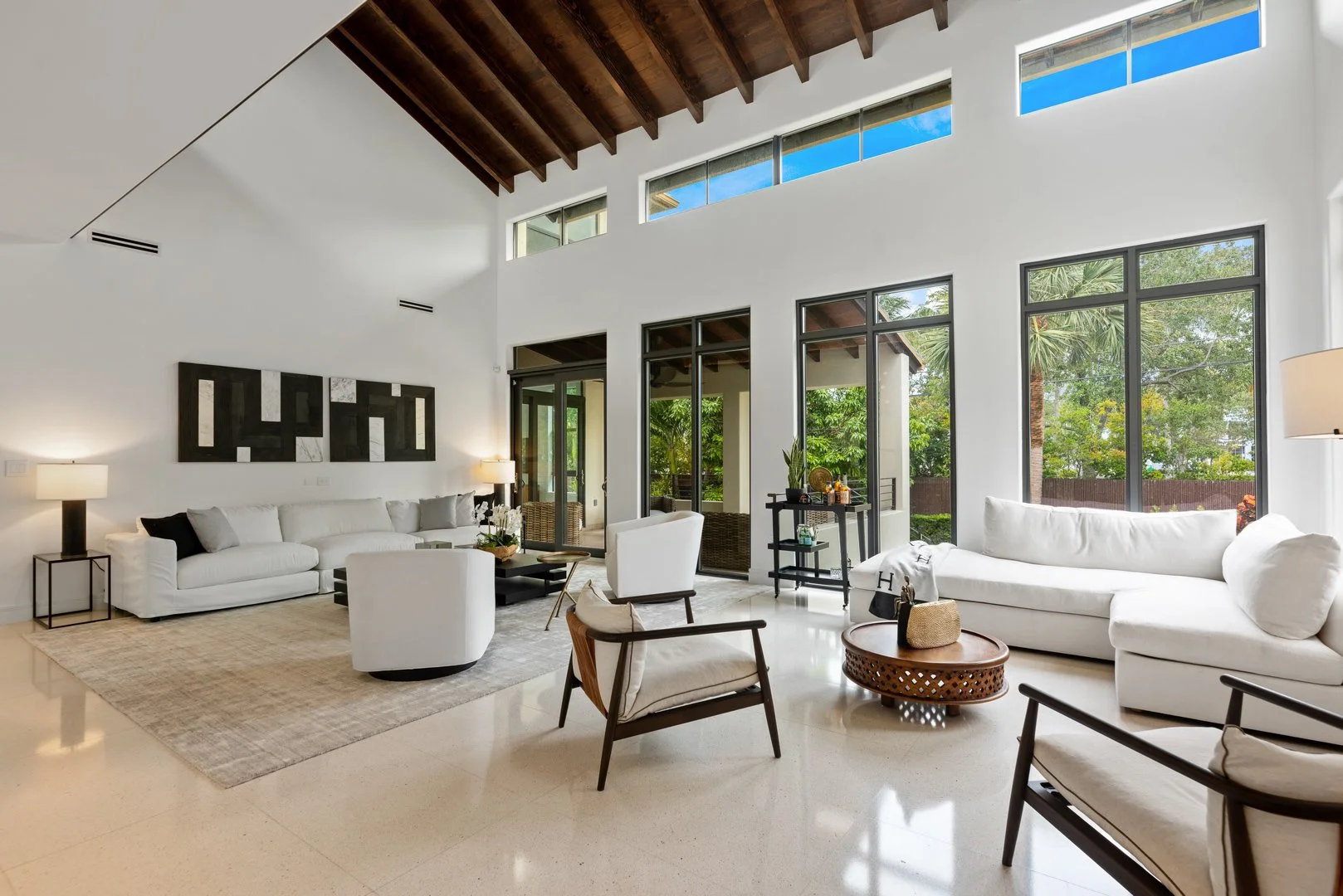 Vaulted living room with exposed dark wood beams, white sofas, dark wood lounge chairs, and clerestory windows in Key Biscayne, Interior Design by CURATED.