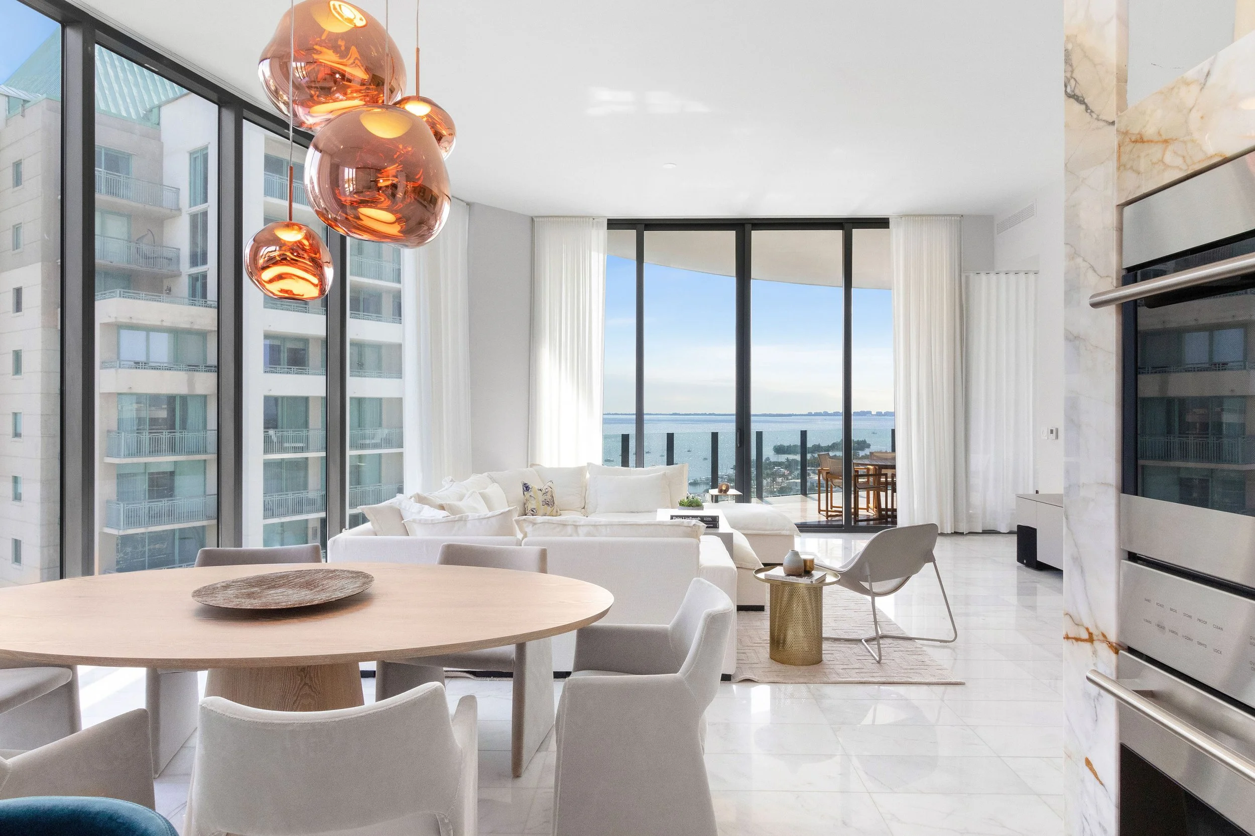 Dining area with copper pendant lights and bay views in Coconut Grove, Interior Design by CURATED.